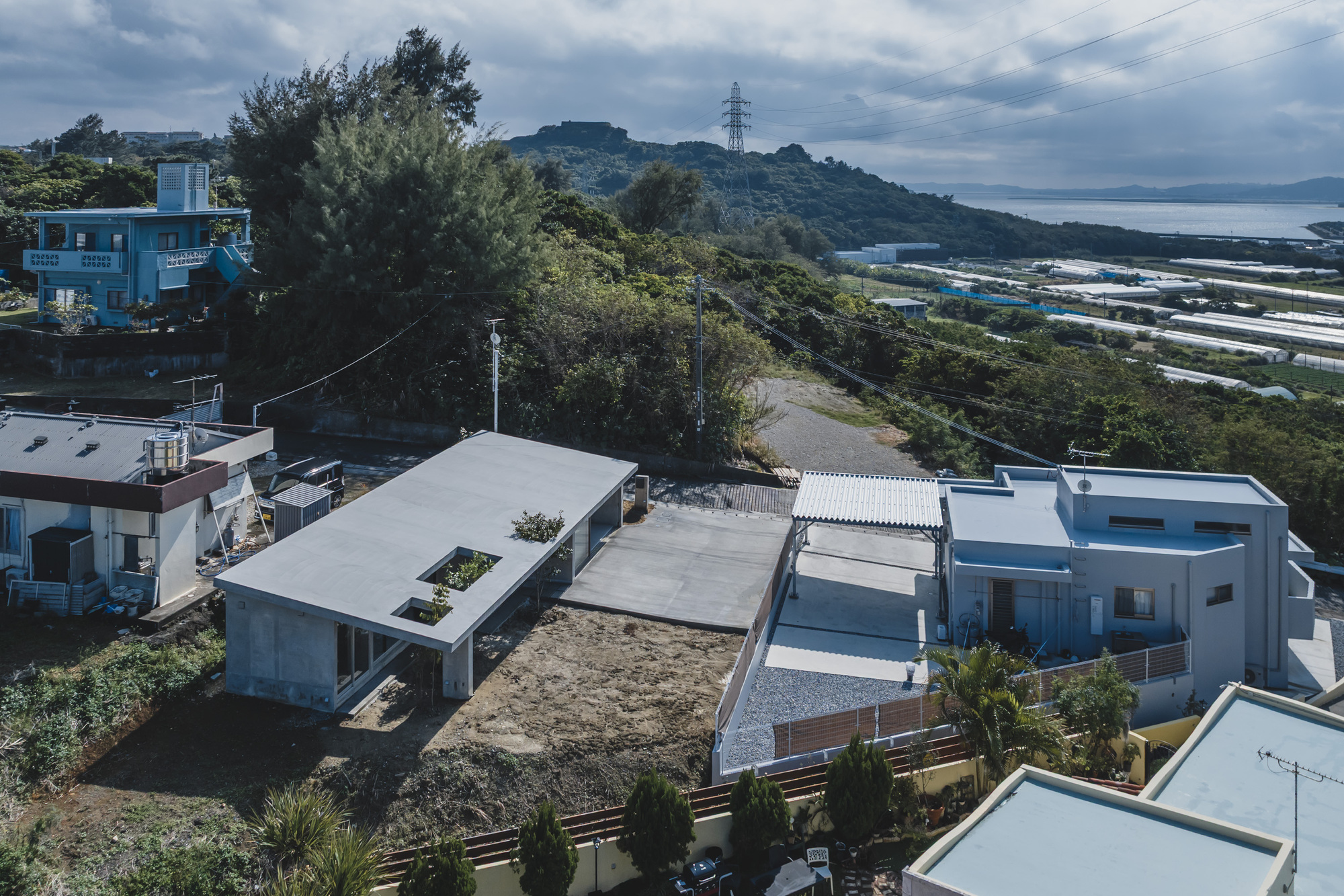 Aerial view of low-slung concrete volumes with flat roofs and planted courtyards among coastal residential development