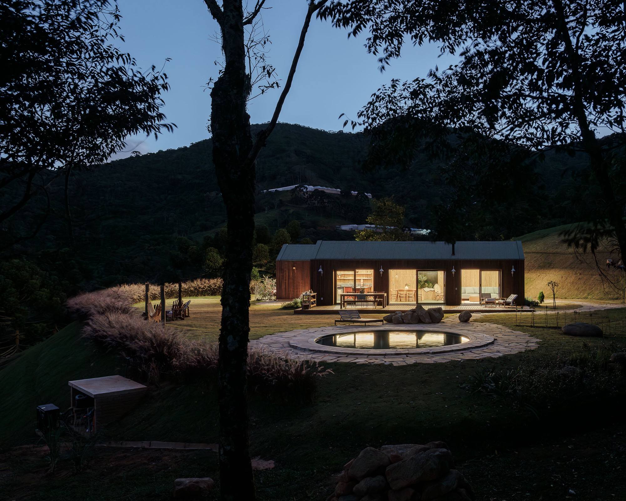 Evening view of the glass-walled pavilion with timber cladding framed by eucalyptus trees and a circular reflecting pool