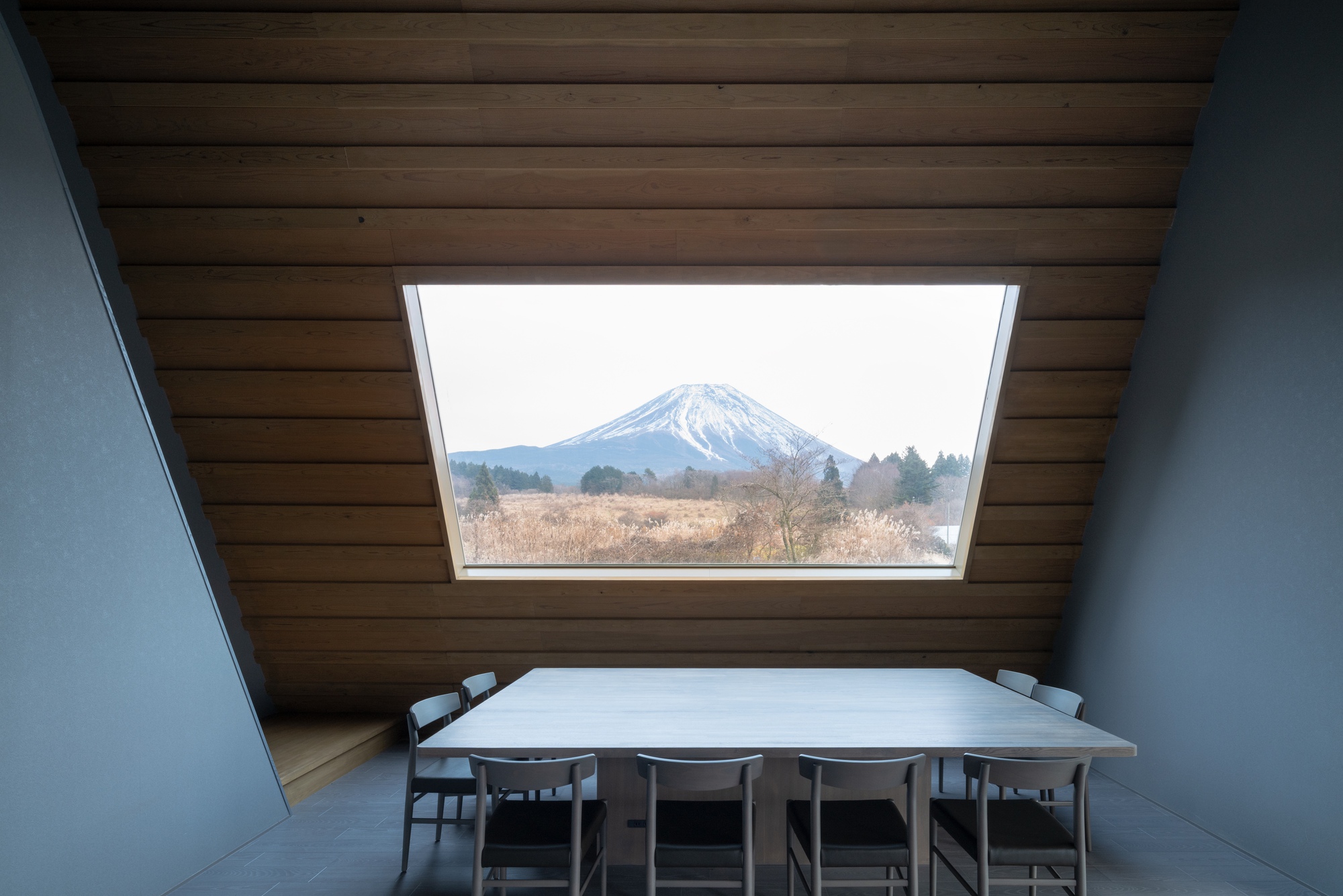 Dining table beneath a rectangular skylight framing view of snowy mountain
