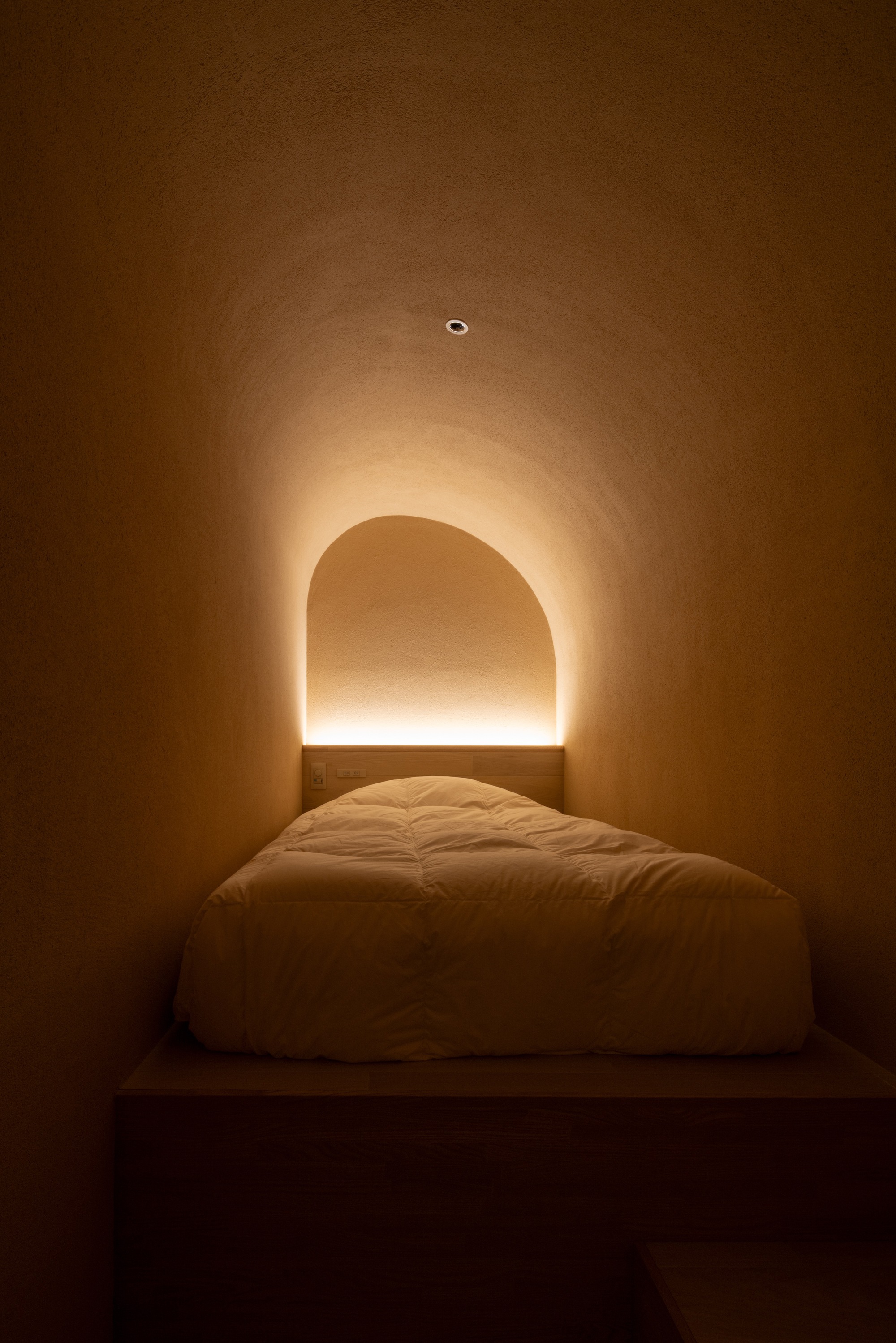 Bedroom alcove with arched niche and concealed linear lighting glowing above the platform bed at night