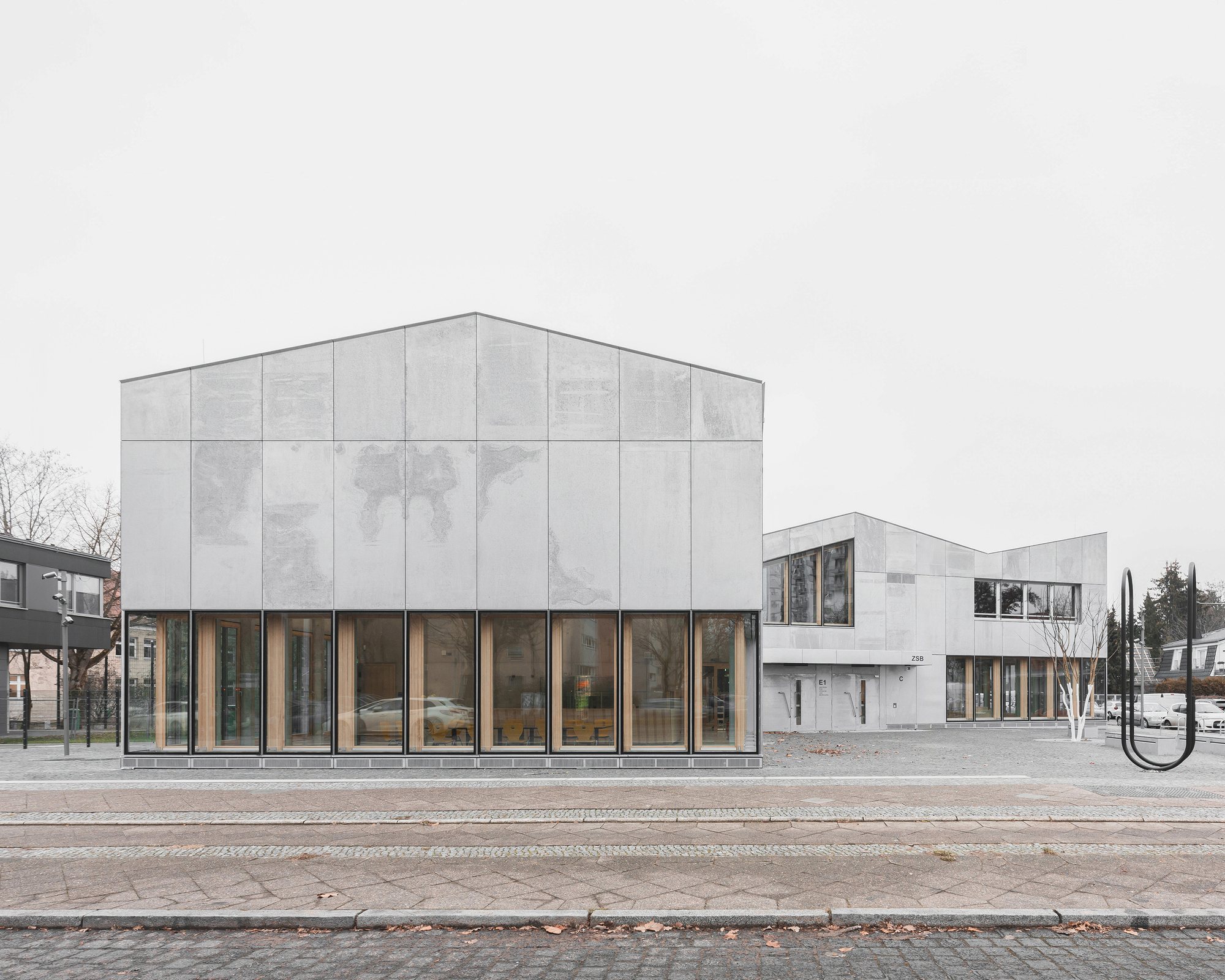 Street view of paneled concrete facade volumes with tall glazed ground floor openings on a grey day
