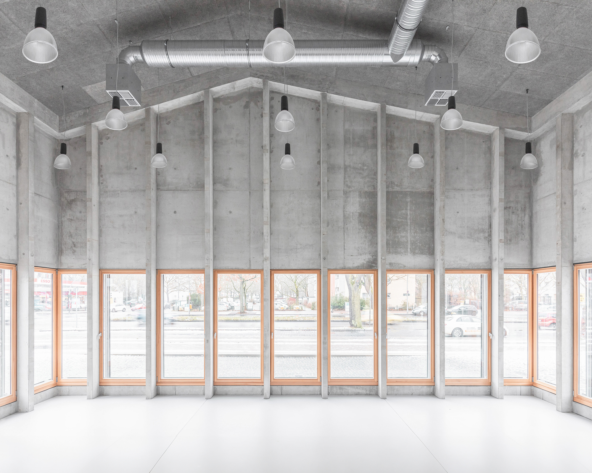 Curved interior corner with rhythmic concrete fins between timber-framed windows under exposed ductwork and pendant lights