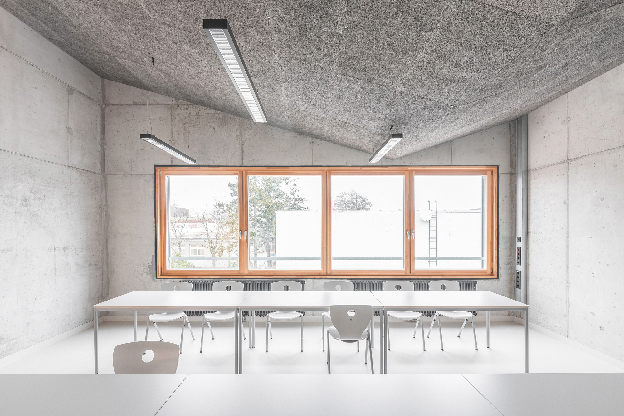 Classroom with paired tables and chairs facing a continuous window with radiators below the sill