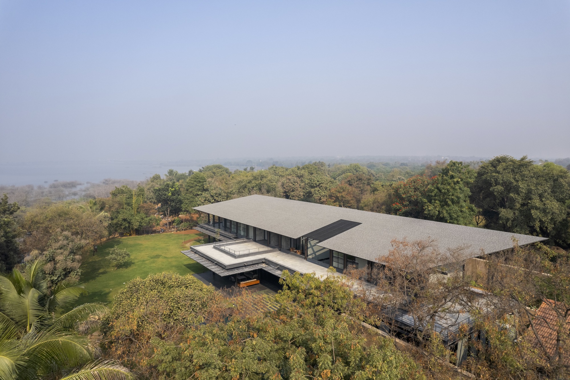 Aerial view of the twin flat roofs over a wooded hillside in misty morning light