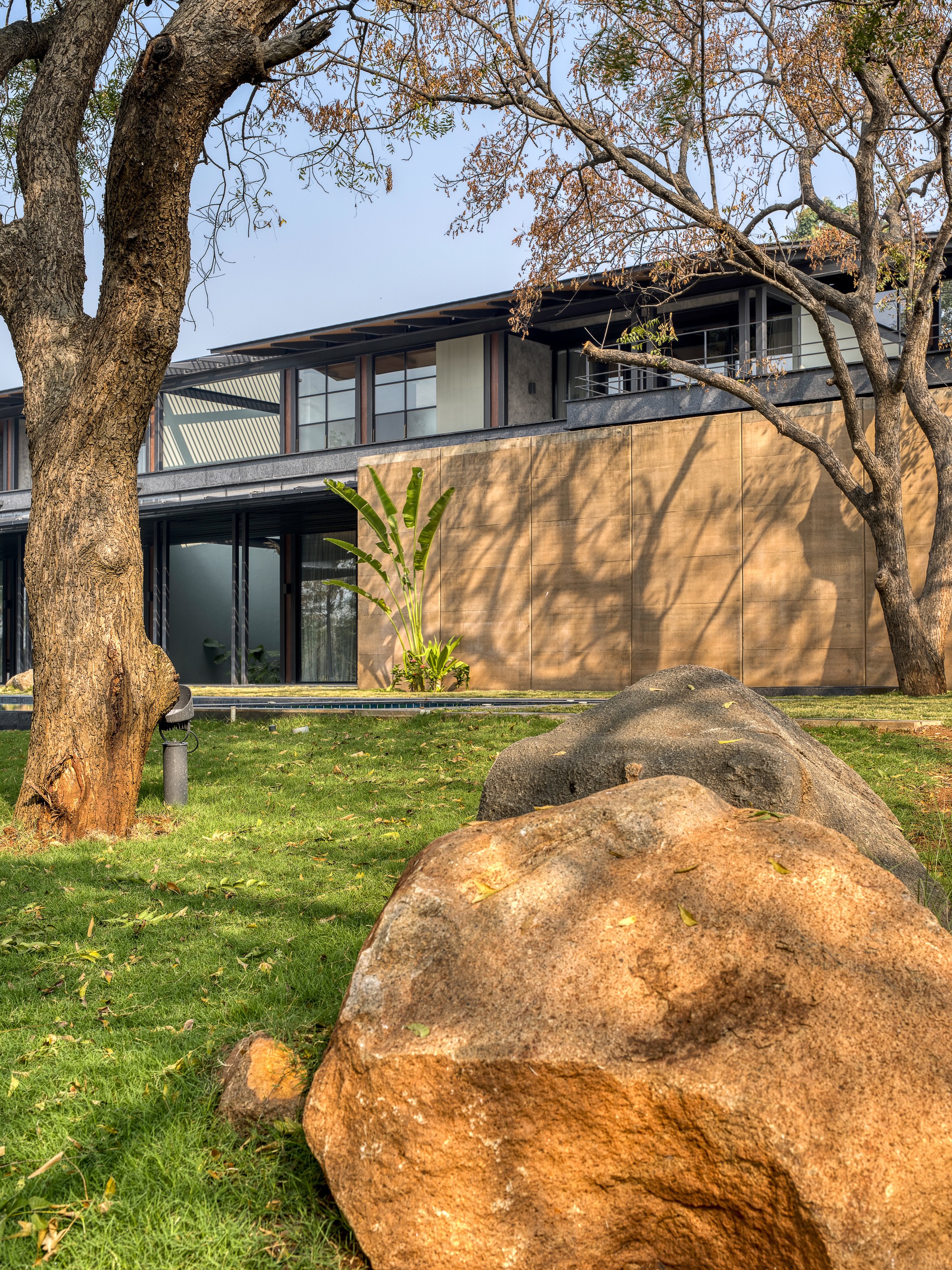 Garden view of the upper terrace and plastered wall framed by a bare tree and granite boulder