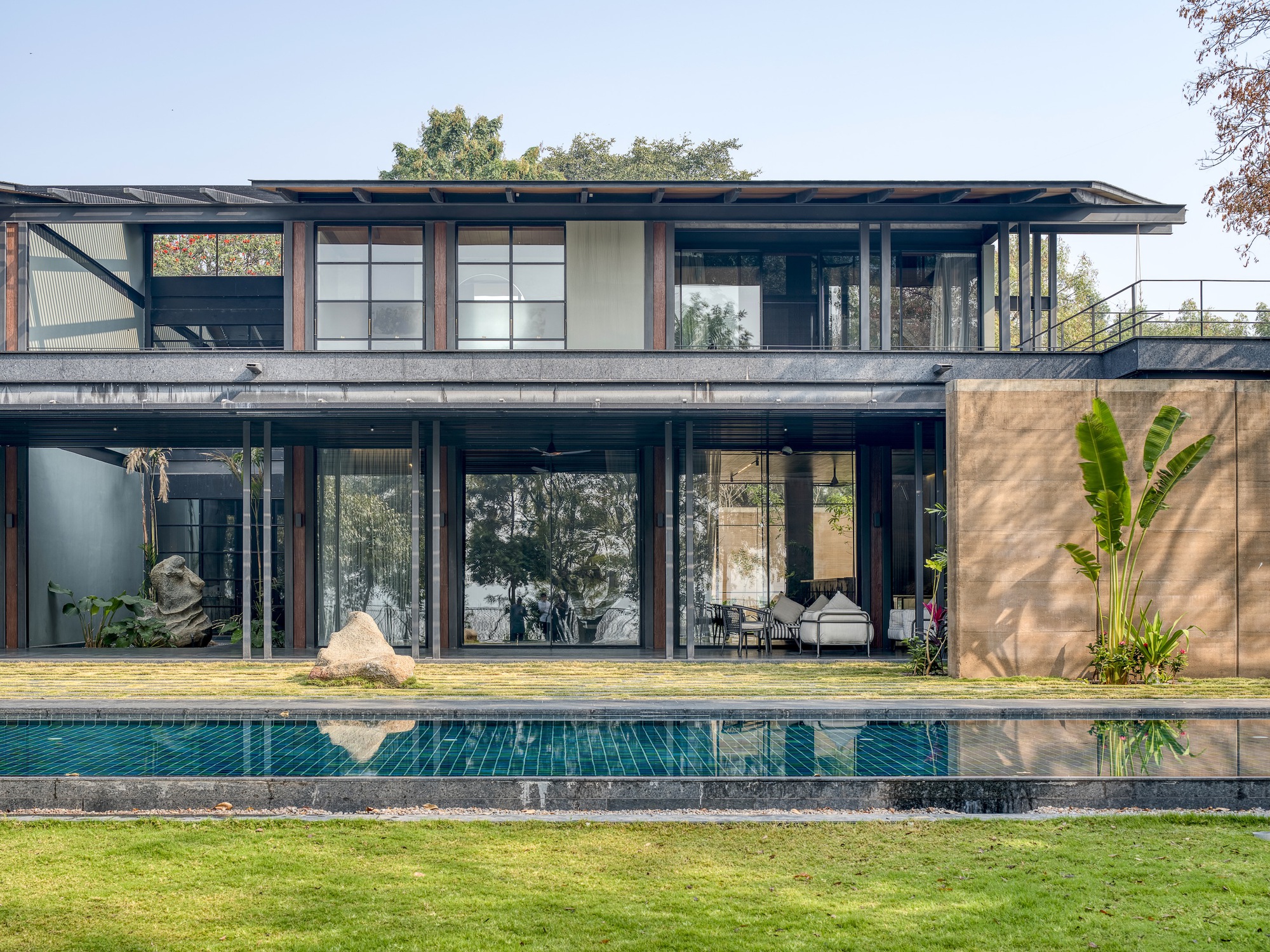 Garden facade with full-height glazing, steel frame and rammed earth wall casting afternoon shadows