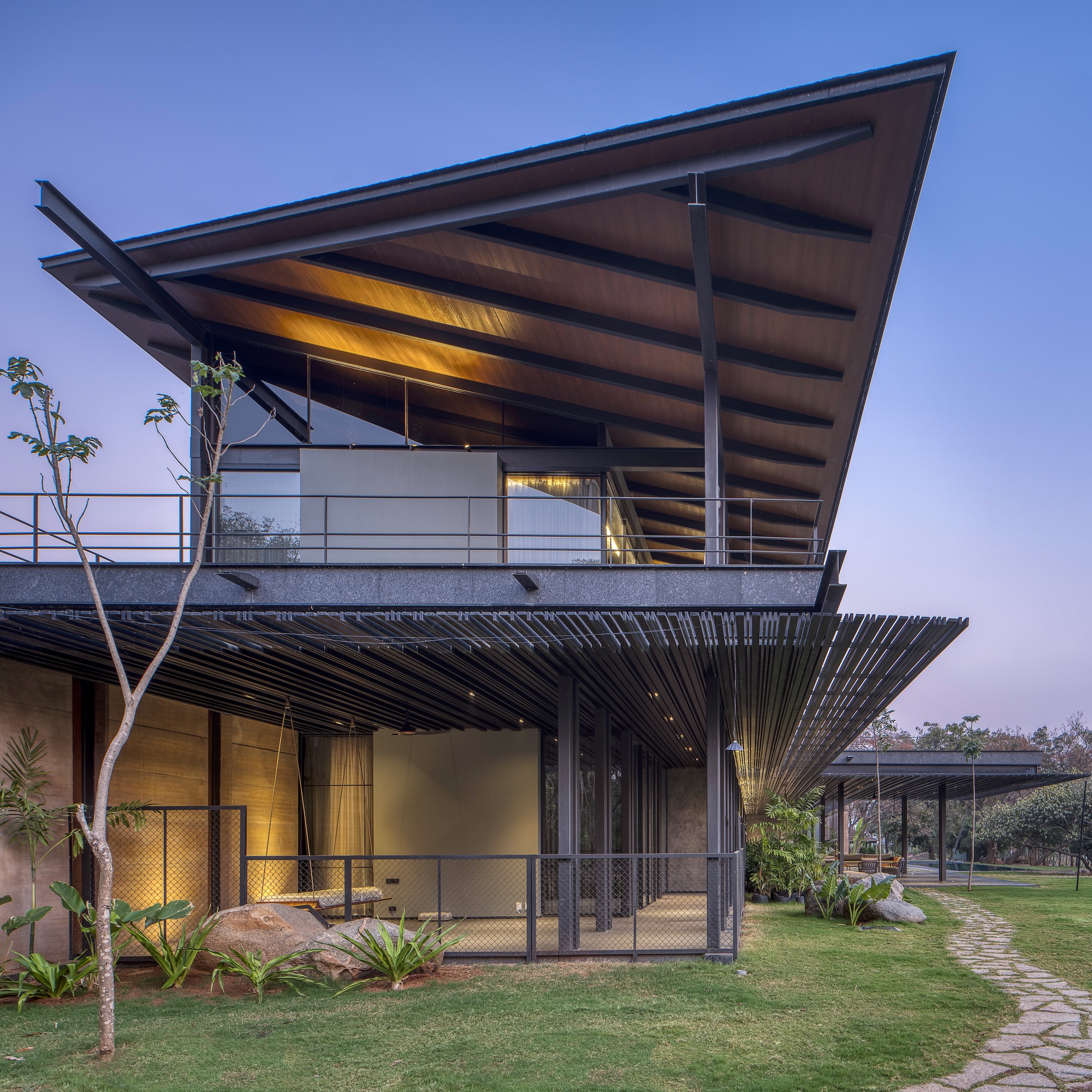 Corner view showing the cantilevered upper balcony with steel columns and horizontal sun louvers below at twilight