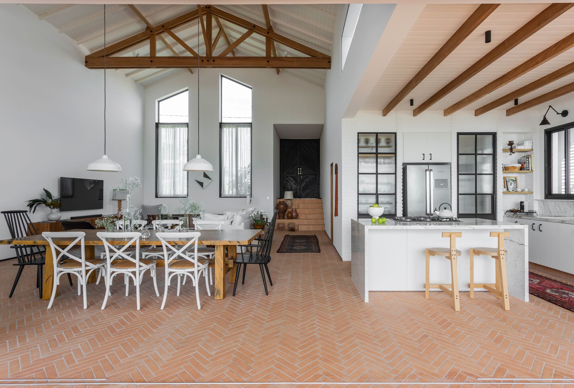 Open-plan living space with herringbone terracotta tile floor and exposed timber trusses overhead