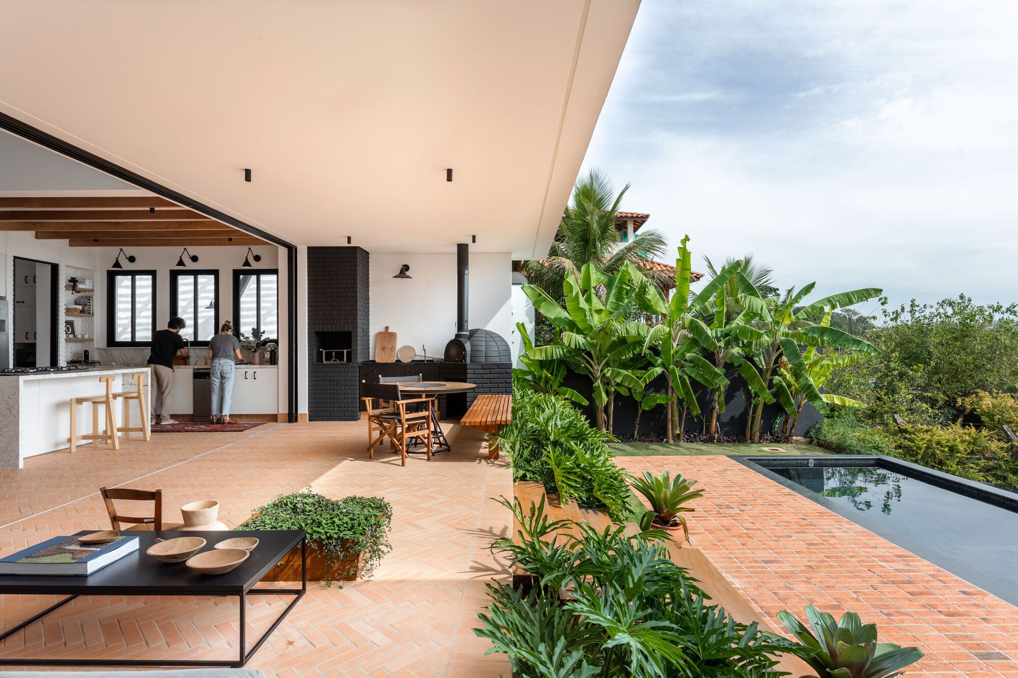 Covered terrace overlooking terracotta-paved deck with planted beds and pool edge