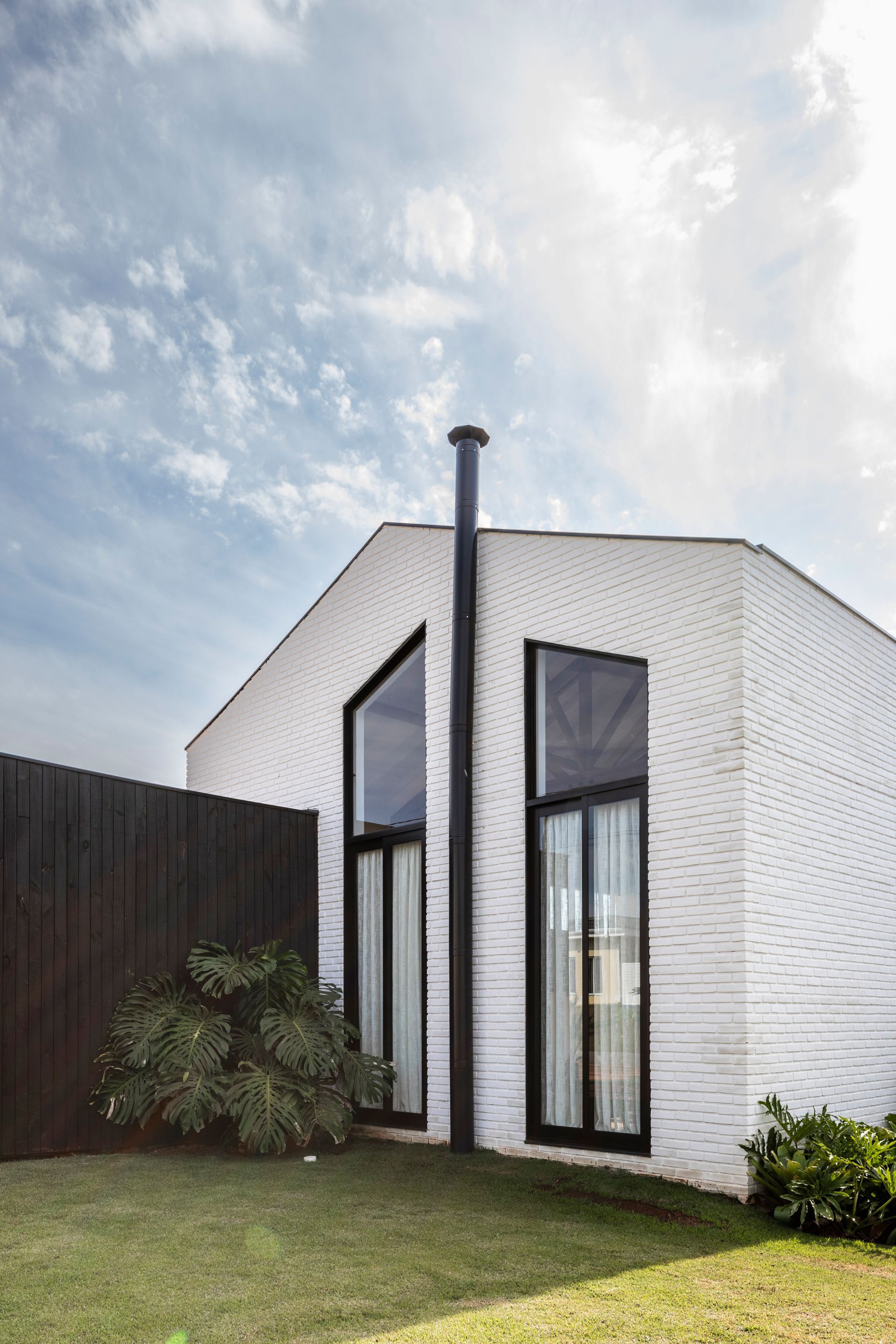 White-painted brick volume with tall black-framed windows and a dark metal flue pipe under cloudy skies