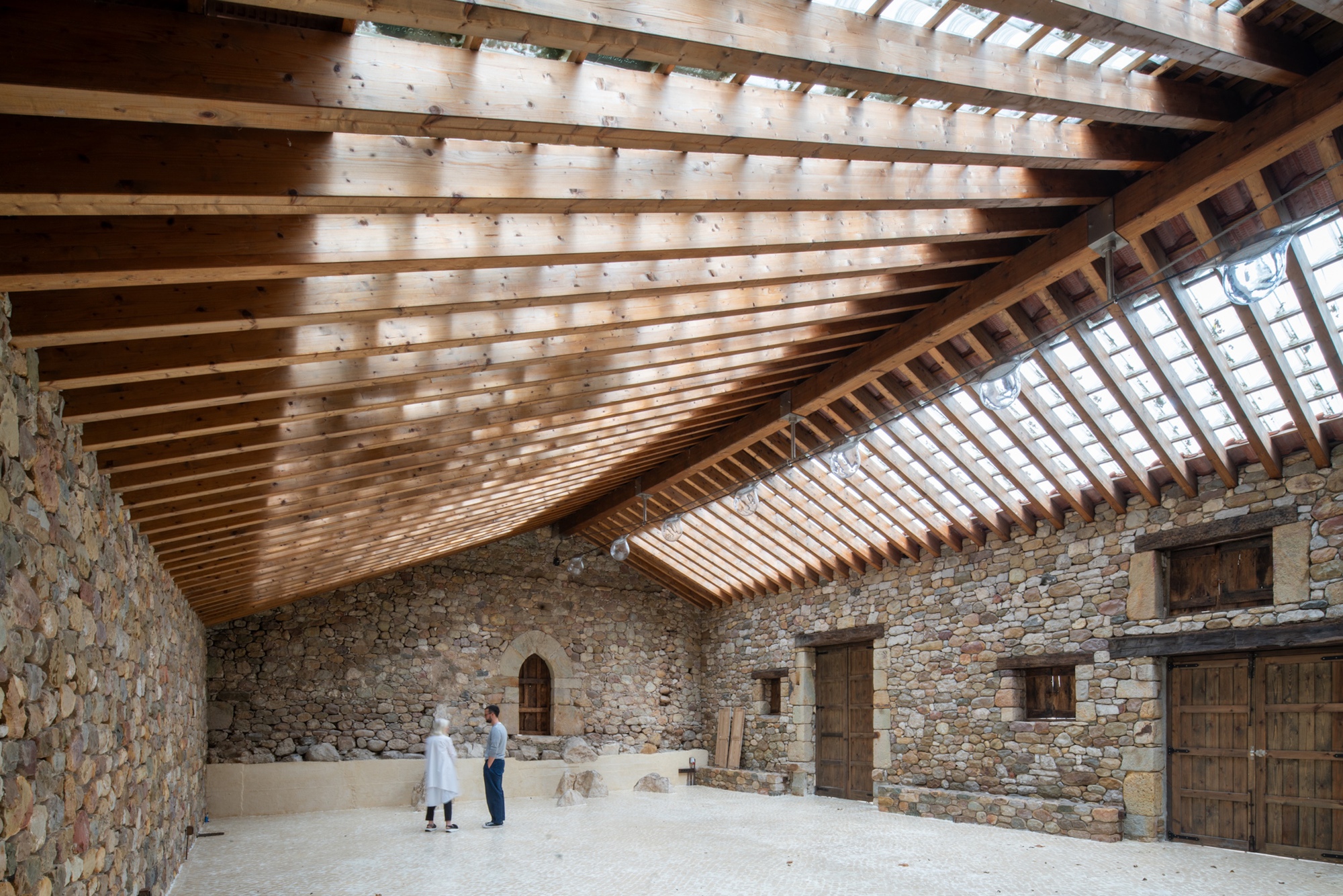 Interior view of the timber rafter roof structure over weathered stone walls with two figures standing below