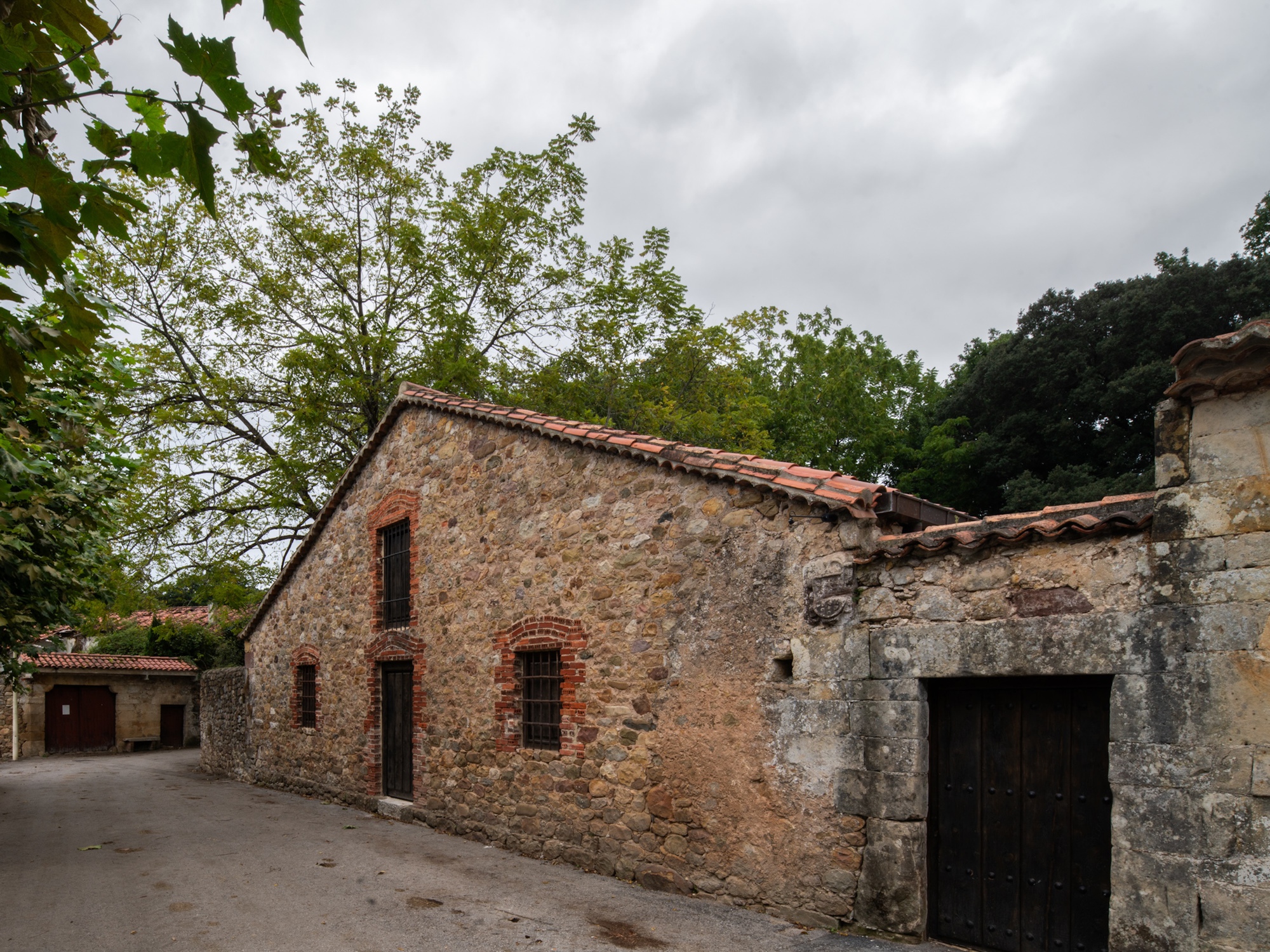 Exterior facade of the weathered stone barn with terra cotta tile roof under an overcast sky