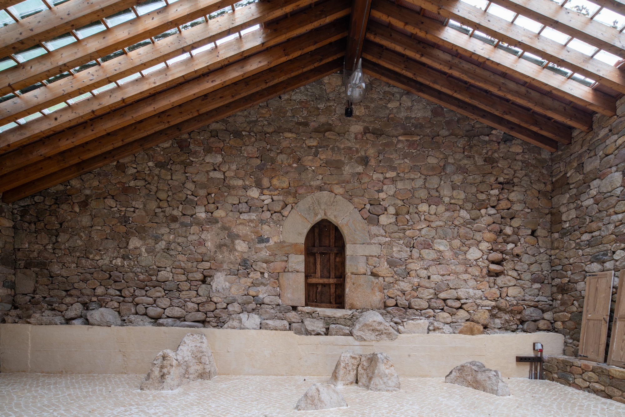 Stone gable end wall with arched timber door and exposed roof rafters above excavated floor level