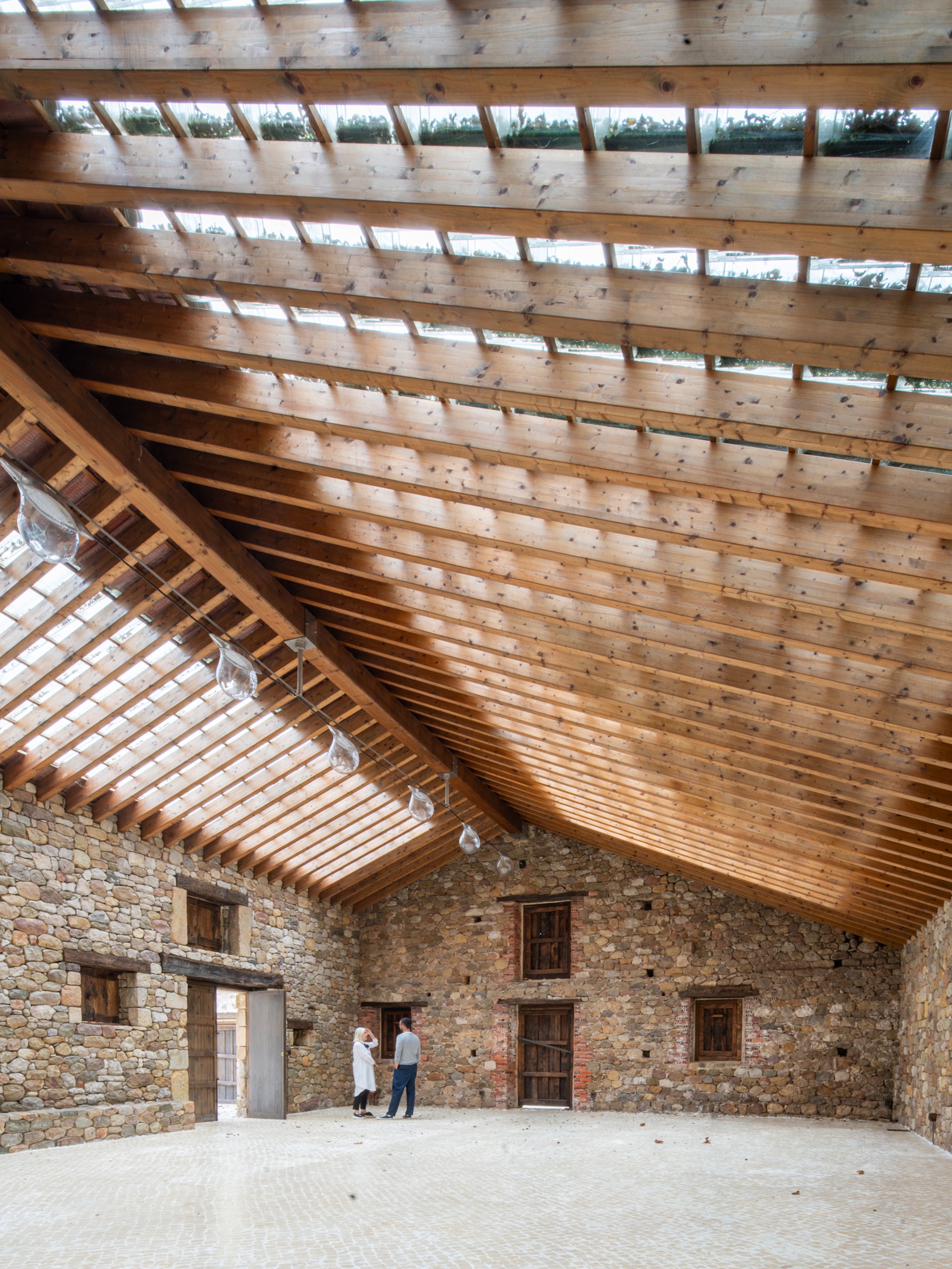 Vaulted timber roof with glazed clerestory openings spanning the stone-walled interior with two visitors conversing