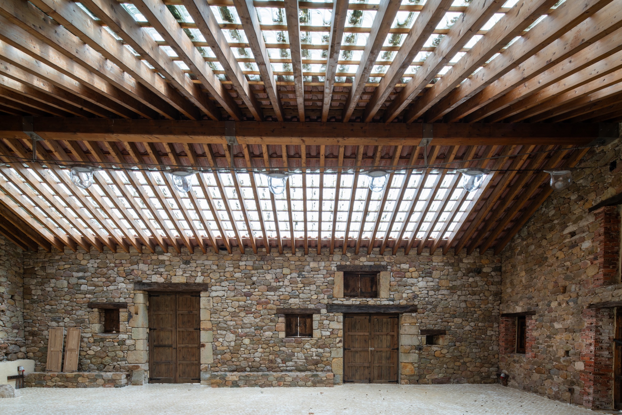View of the slatted timber roof structure with rectangular skylights above the stone wall and timber doors