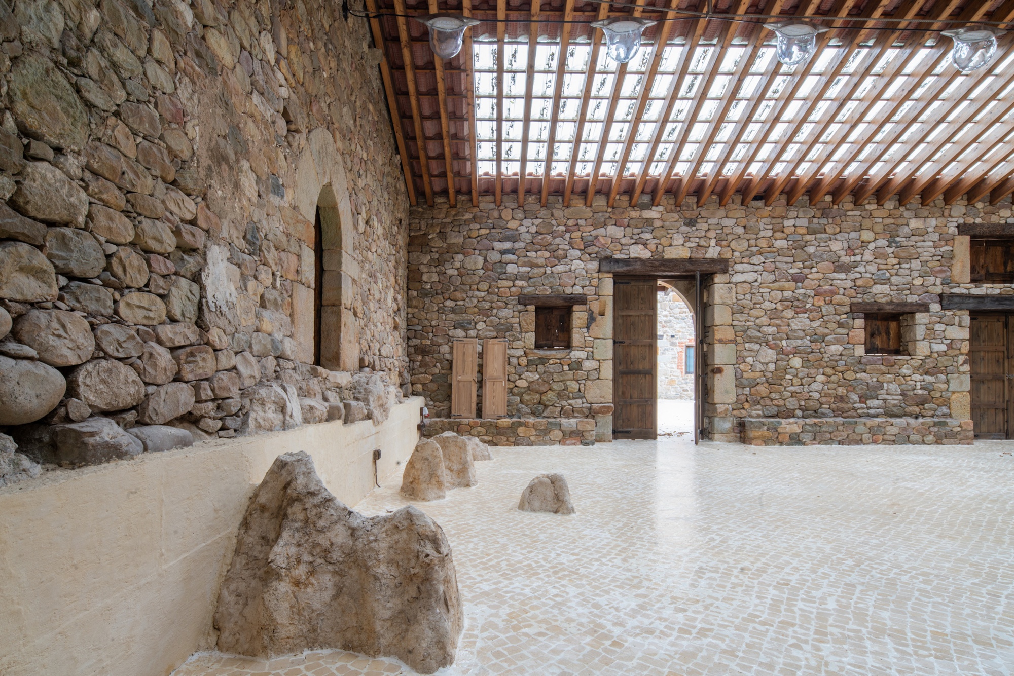 Stone-walled interior with doorways and preserved rock fragments on a pale tile floor