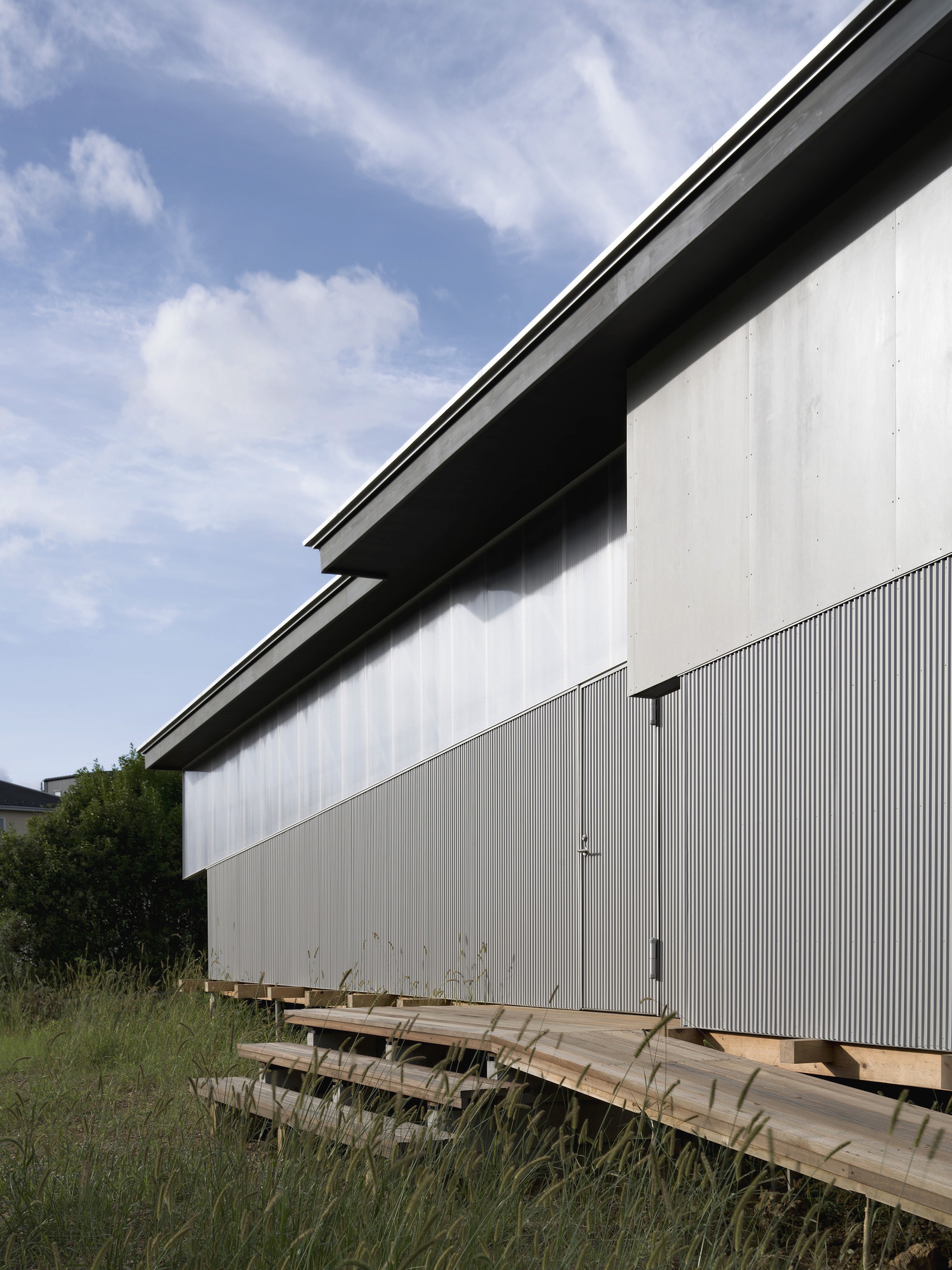 Corrugated metal facade with timber deck elevated on concrete blocks beneath a blue sky