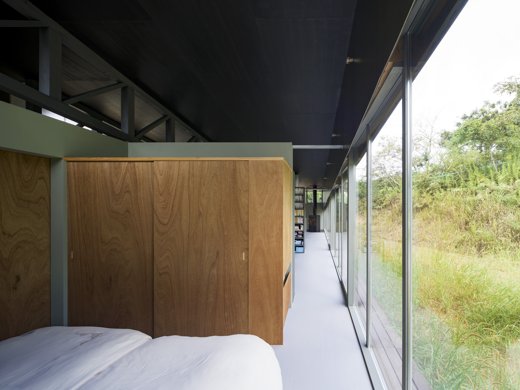 Bedroom with timber wardrobe and full-height glazing overlooking meadow grasses in afternoon light