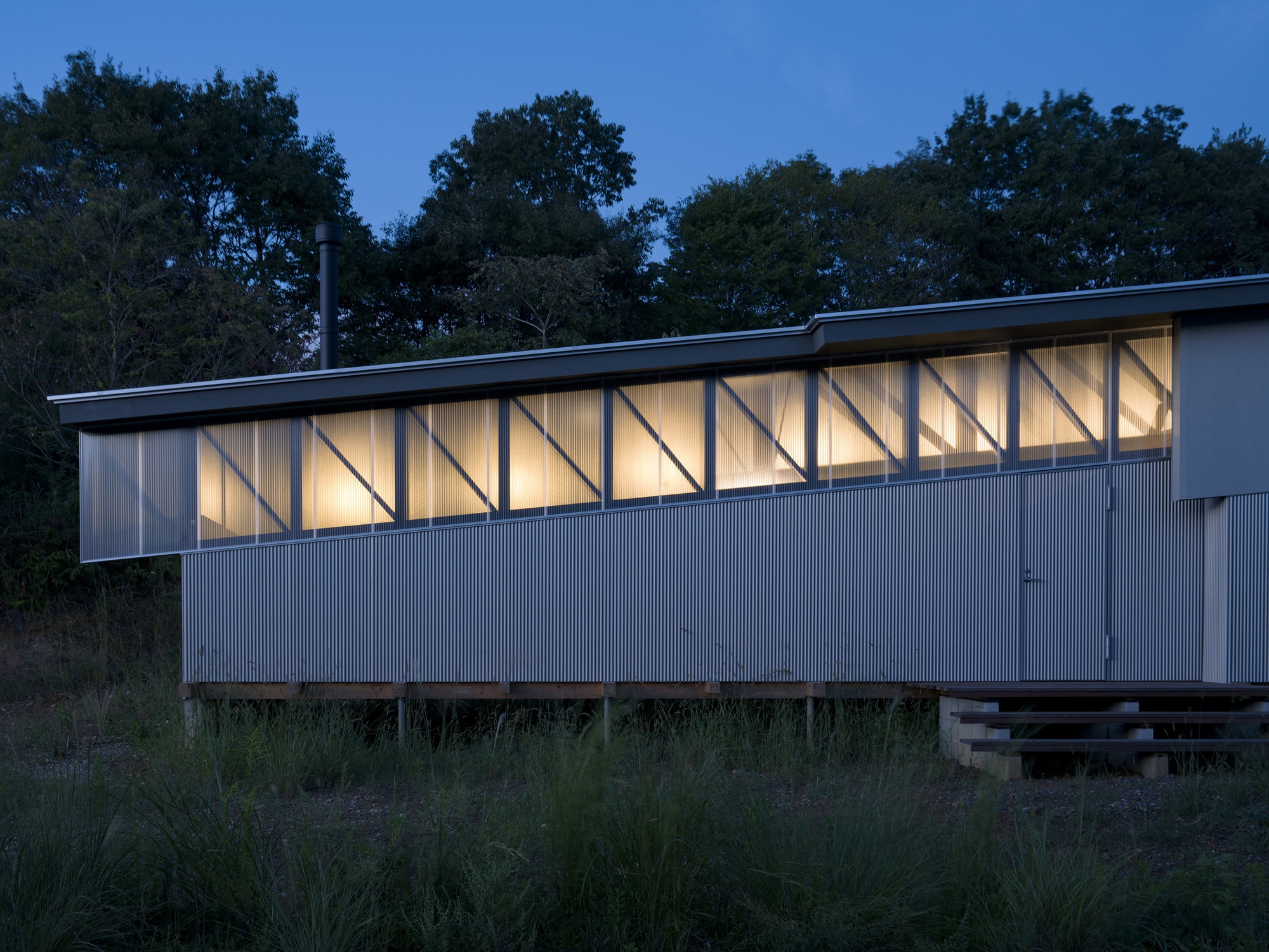 Illuminated facade with exposed diagonal timber framing and corrugated metal cladding at dusk