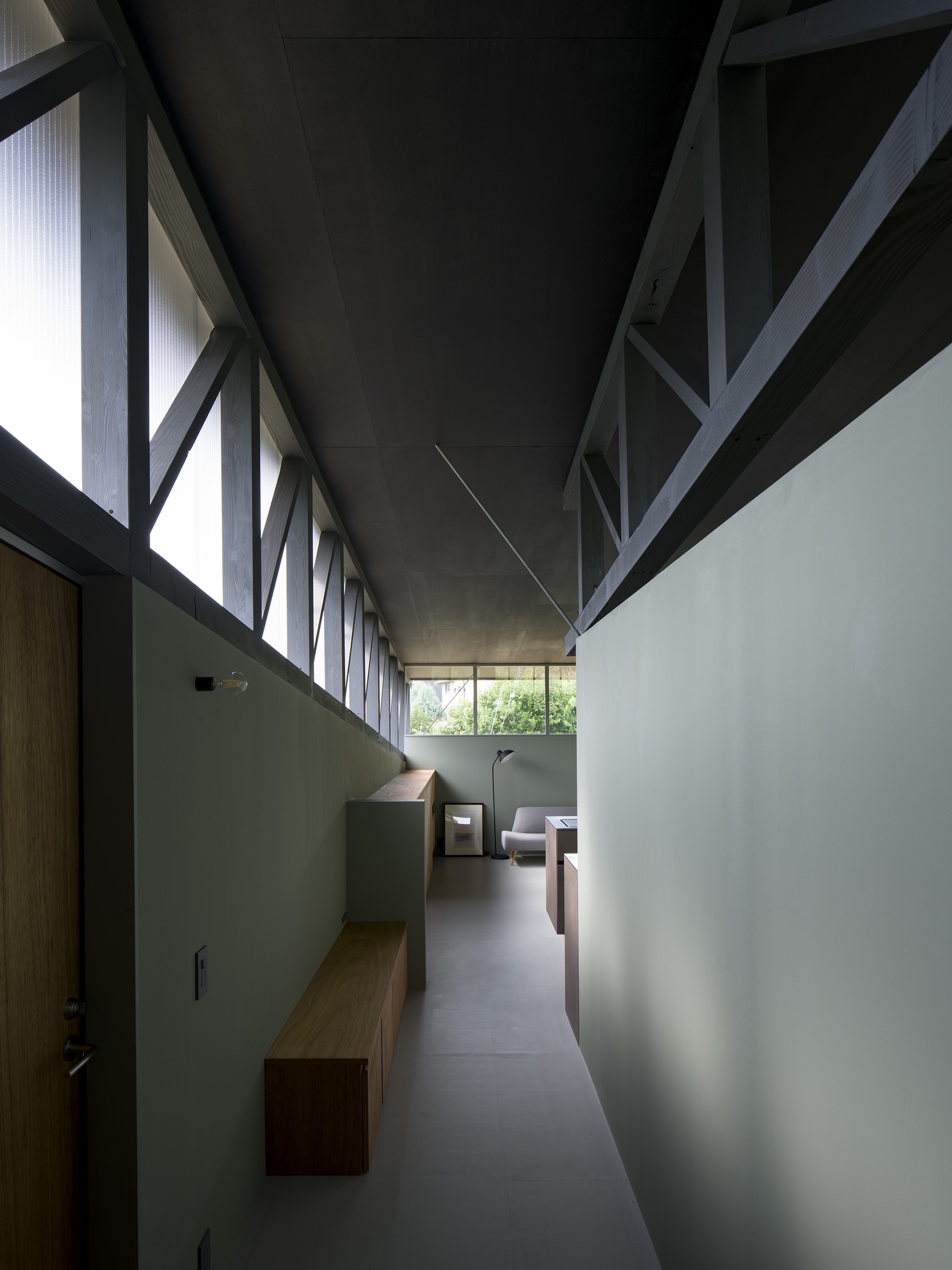 Corridor with exposed diagonal timber bracing overhead and pale green walls leading to seating area
