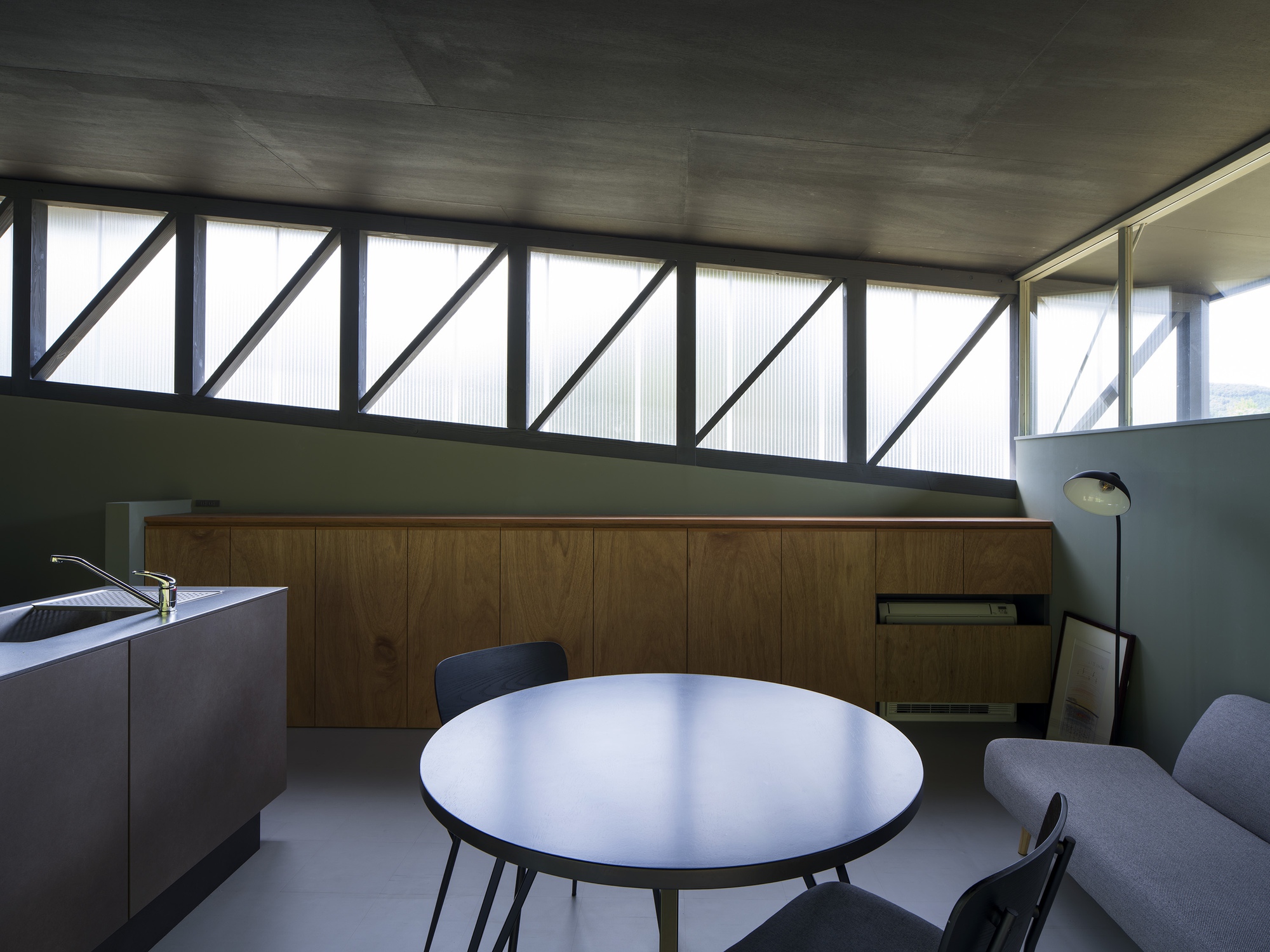 Interior dining area with diagonal braced clerestory windows and timber cabinetry beneath concrete ceiling