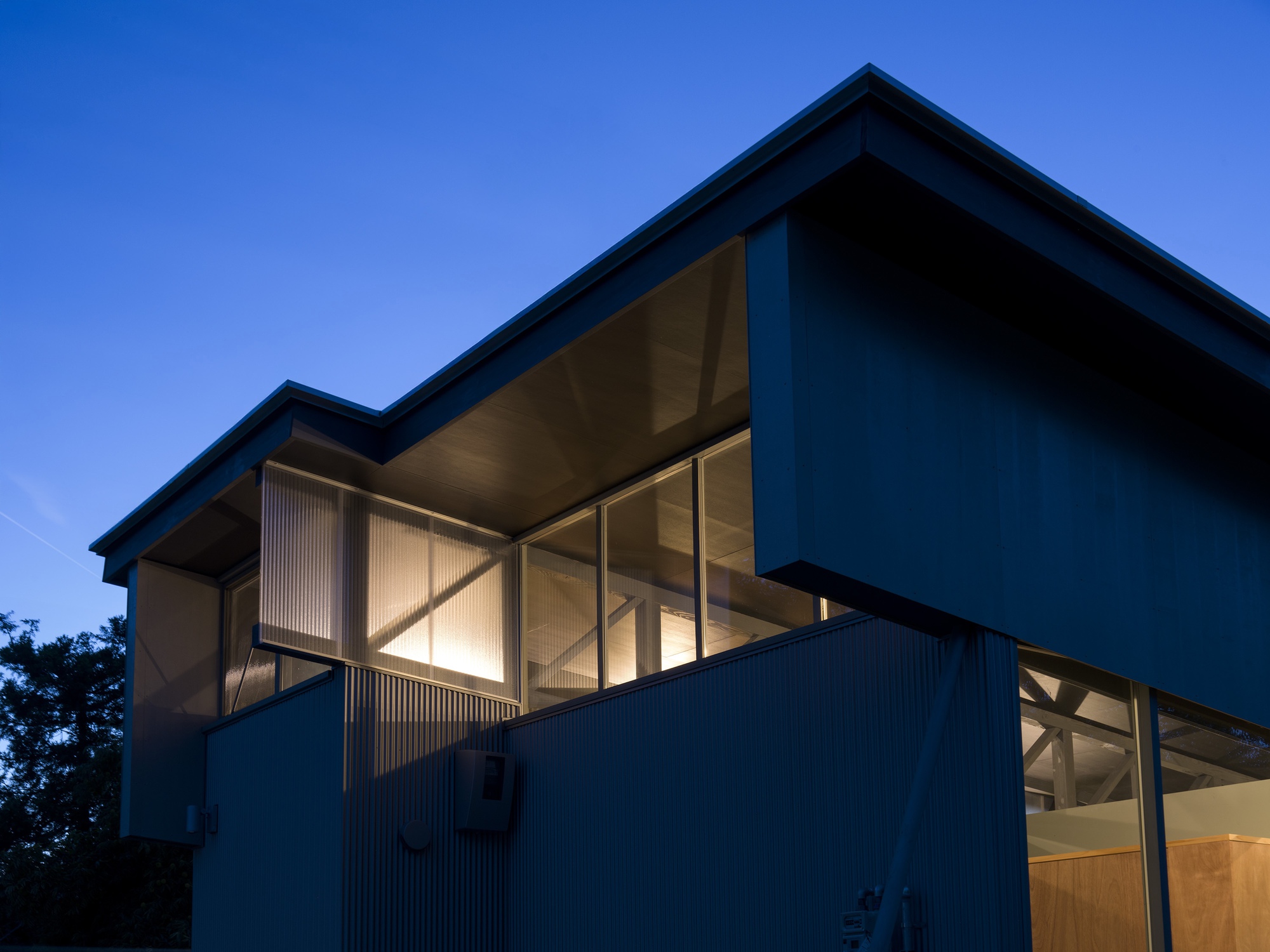 Corner view of the cantilevered upper volume with diagonal braced glazing at twilight