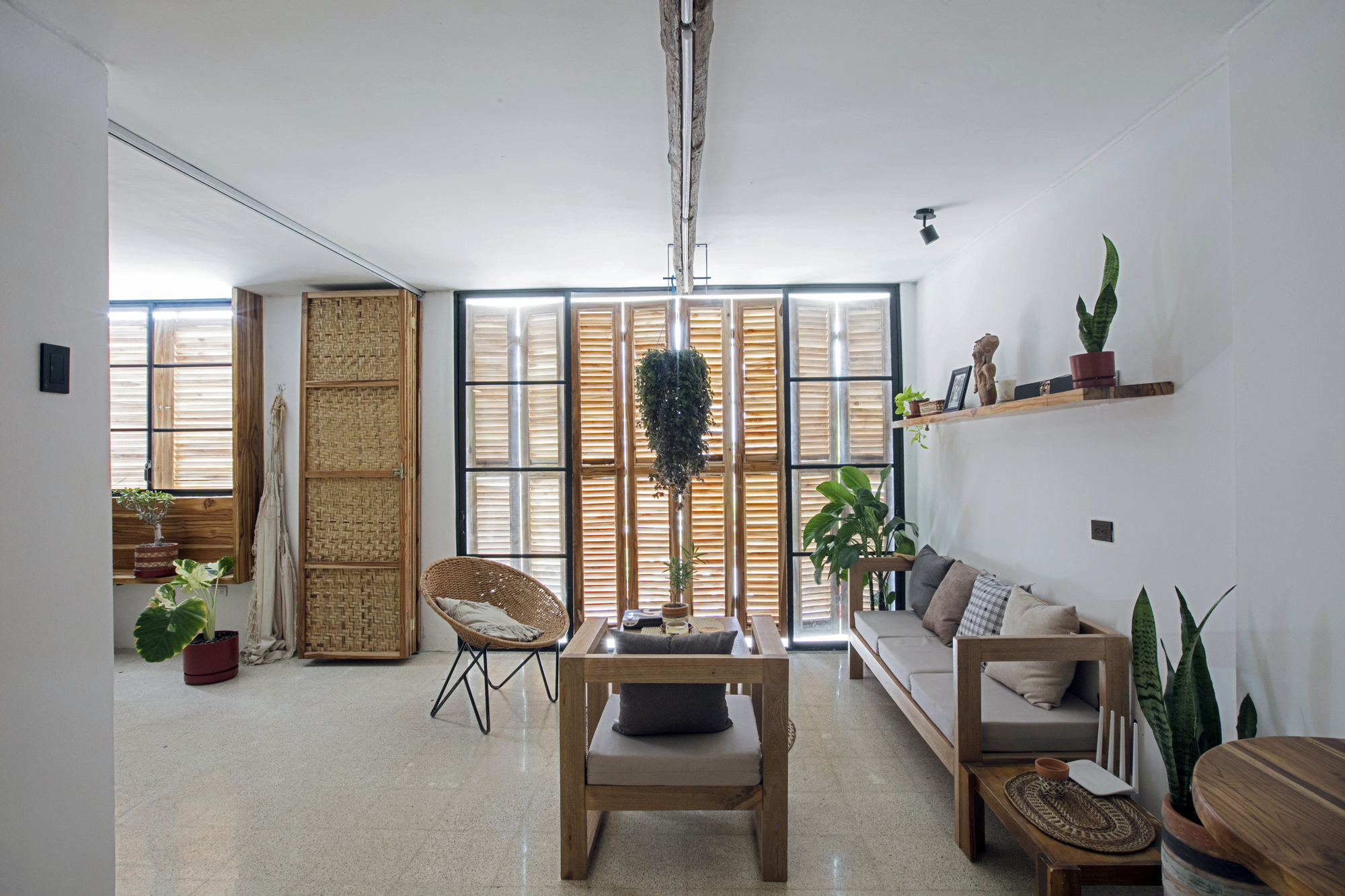Living room with timber louvre screens filtering daylight and woven panels on polished concrete floor