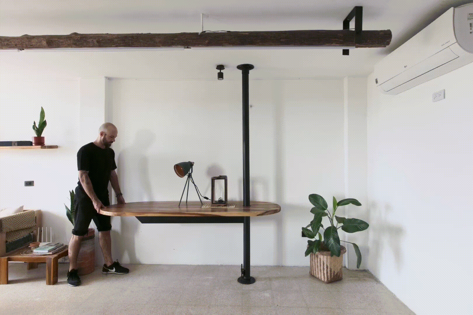 Living room with a fold-down timber table suspended from a black vertical pipe column