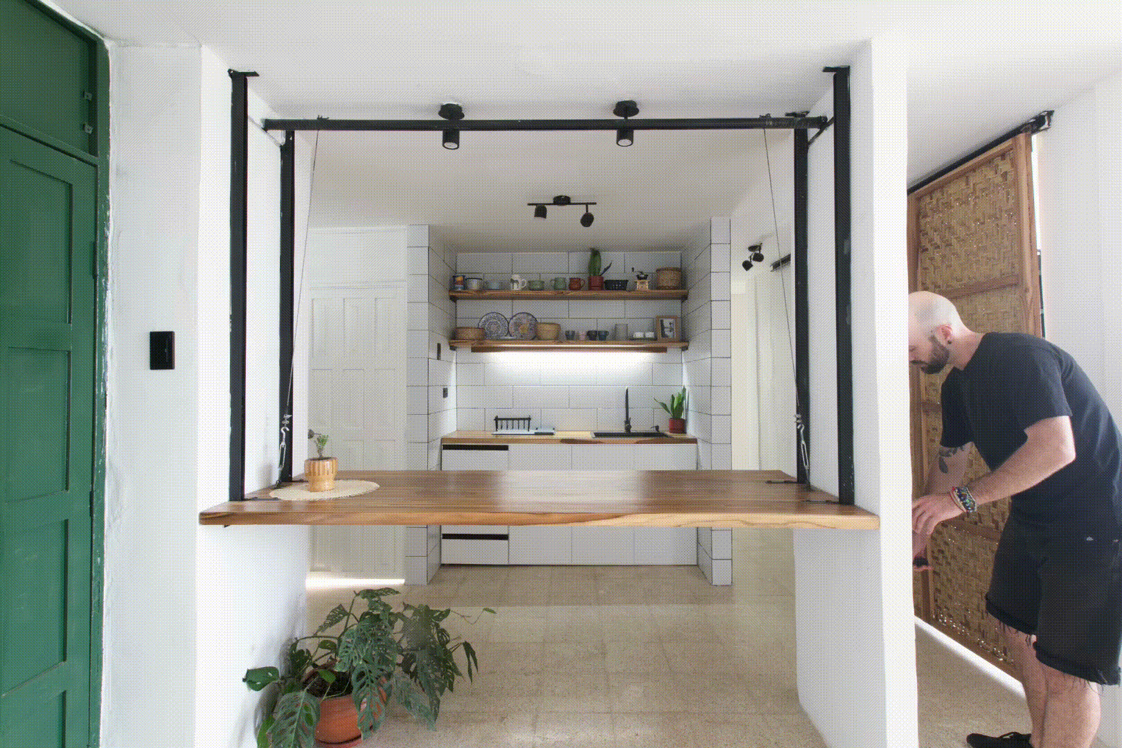 Kitchen opening framed by black steel portal and timber counter with a person standing at the doorway