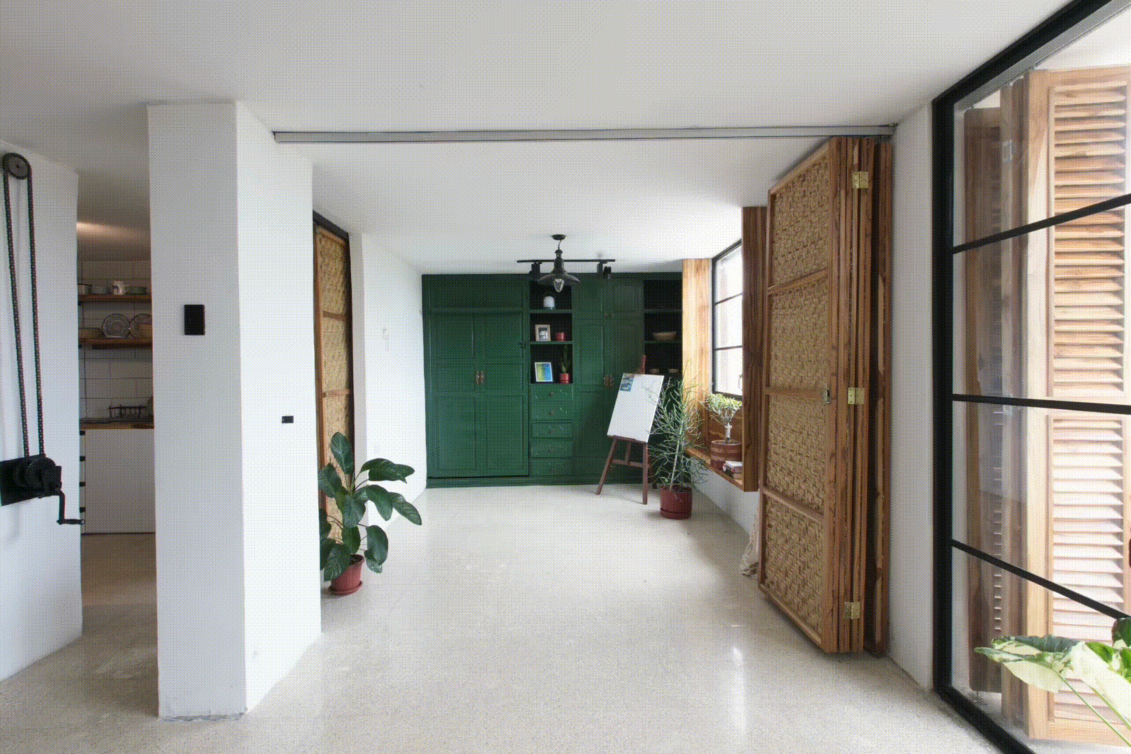 Open-plan interior showing kitchen alcove, woven rattan doors, and polished concrete floors with natural light