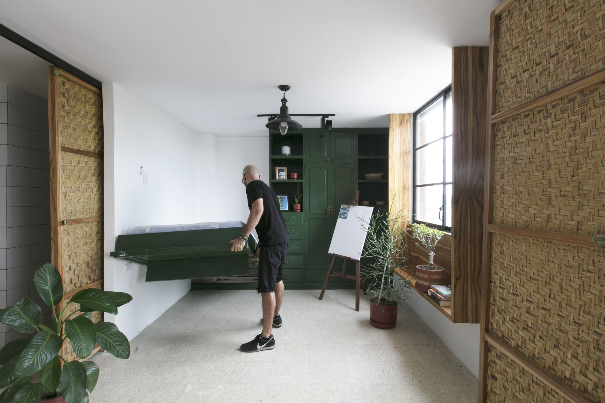 Person unfolding green fold-down bench beside built-in cabinetry and easel in a sunlit hallway