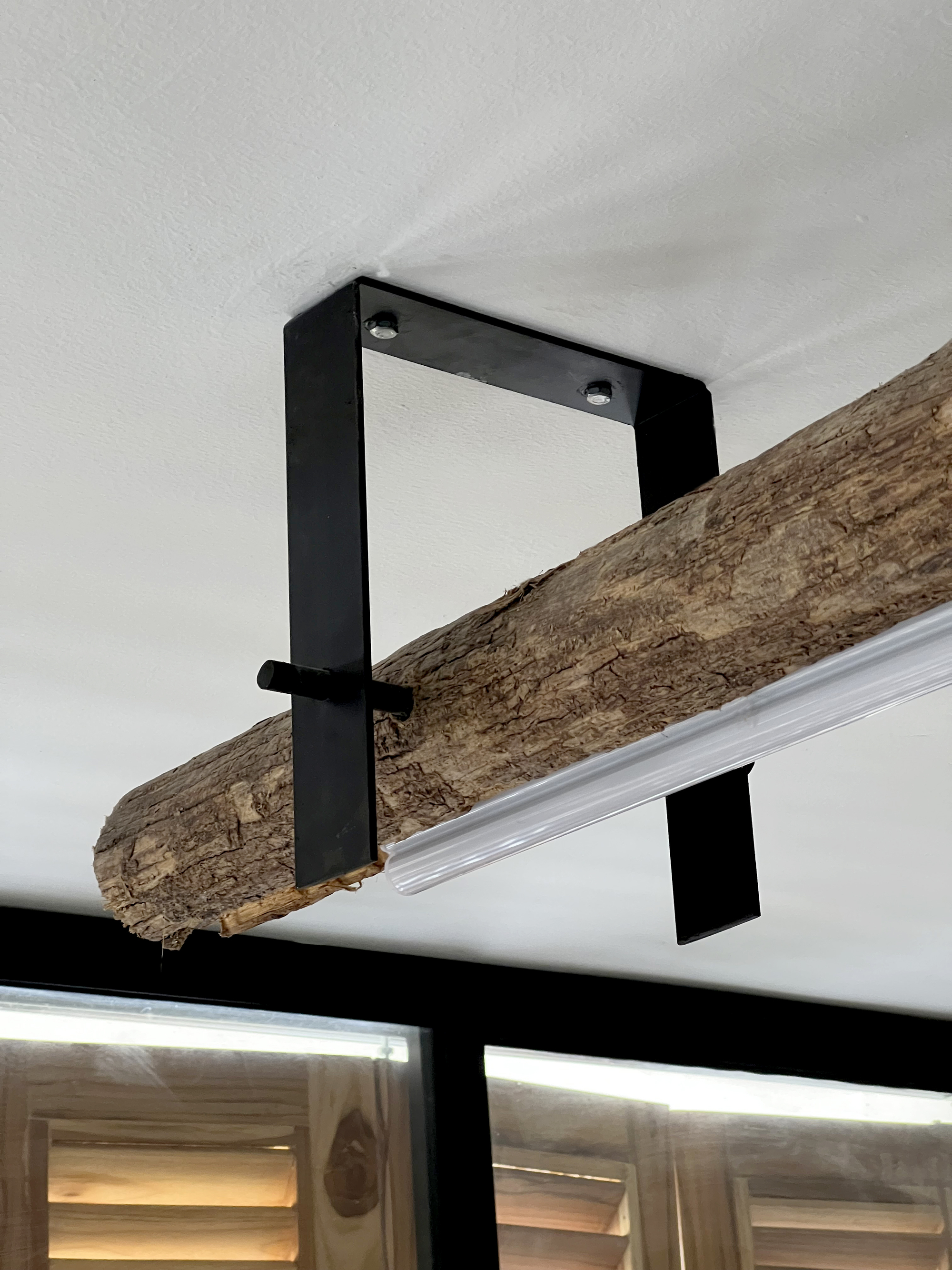 Reclaimed timber beam suspended from the white ceiling by black steel brackets with visible bolts