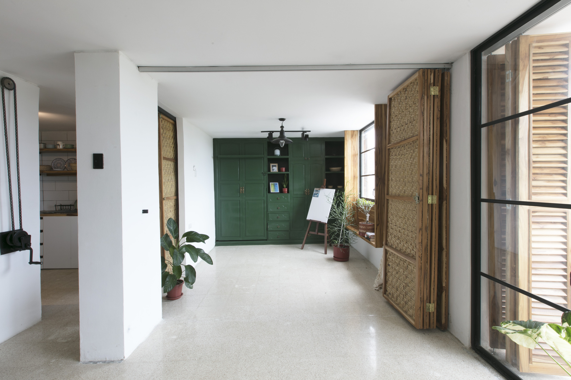 Interior entry hall with terrazzo flooring, green cabinetry, and woven bamboo panels beside glazed doors