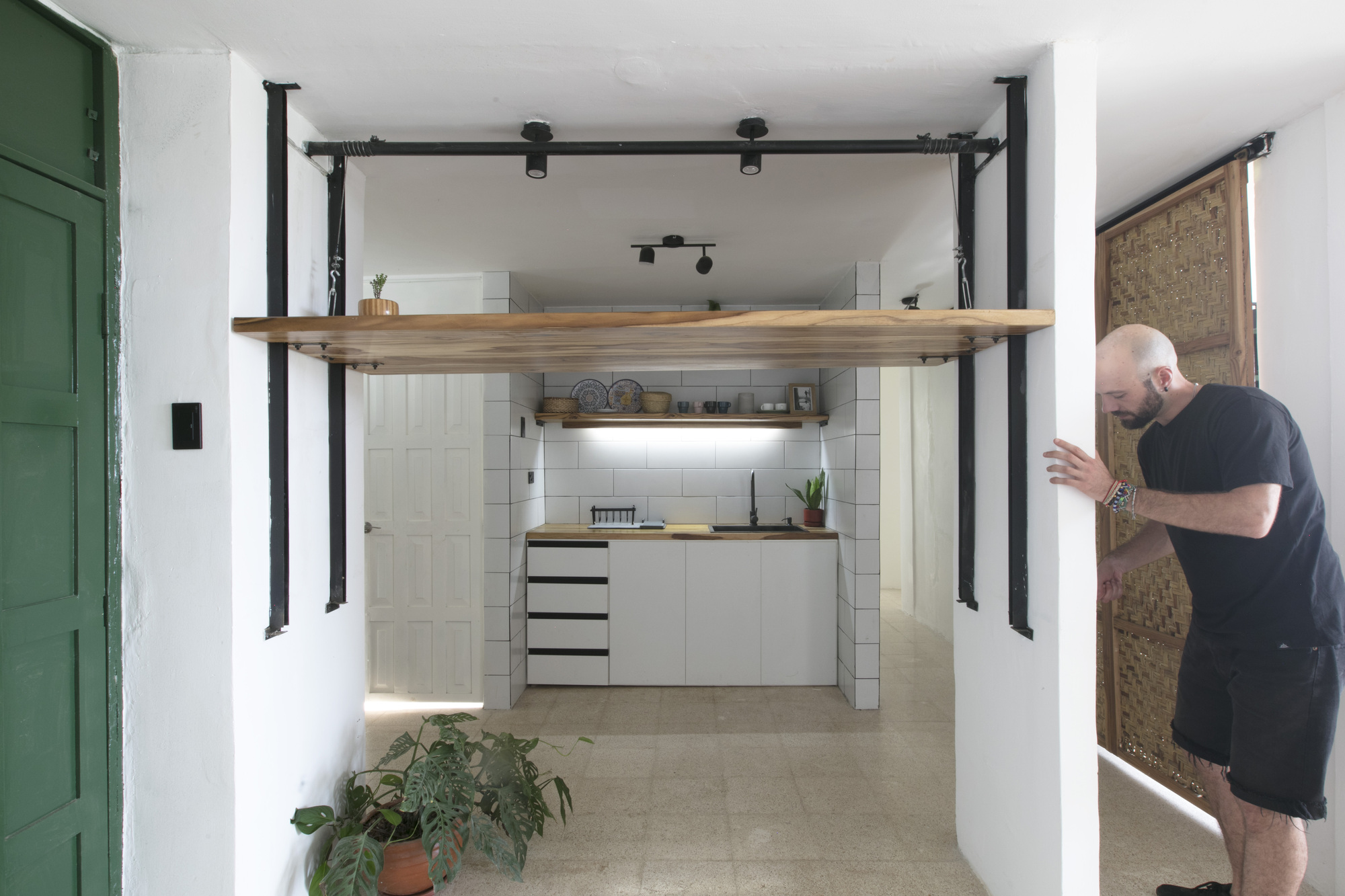 Kitchen alcove with white tile backsplash framed by black steel columns and a timber shelf overhead