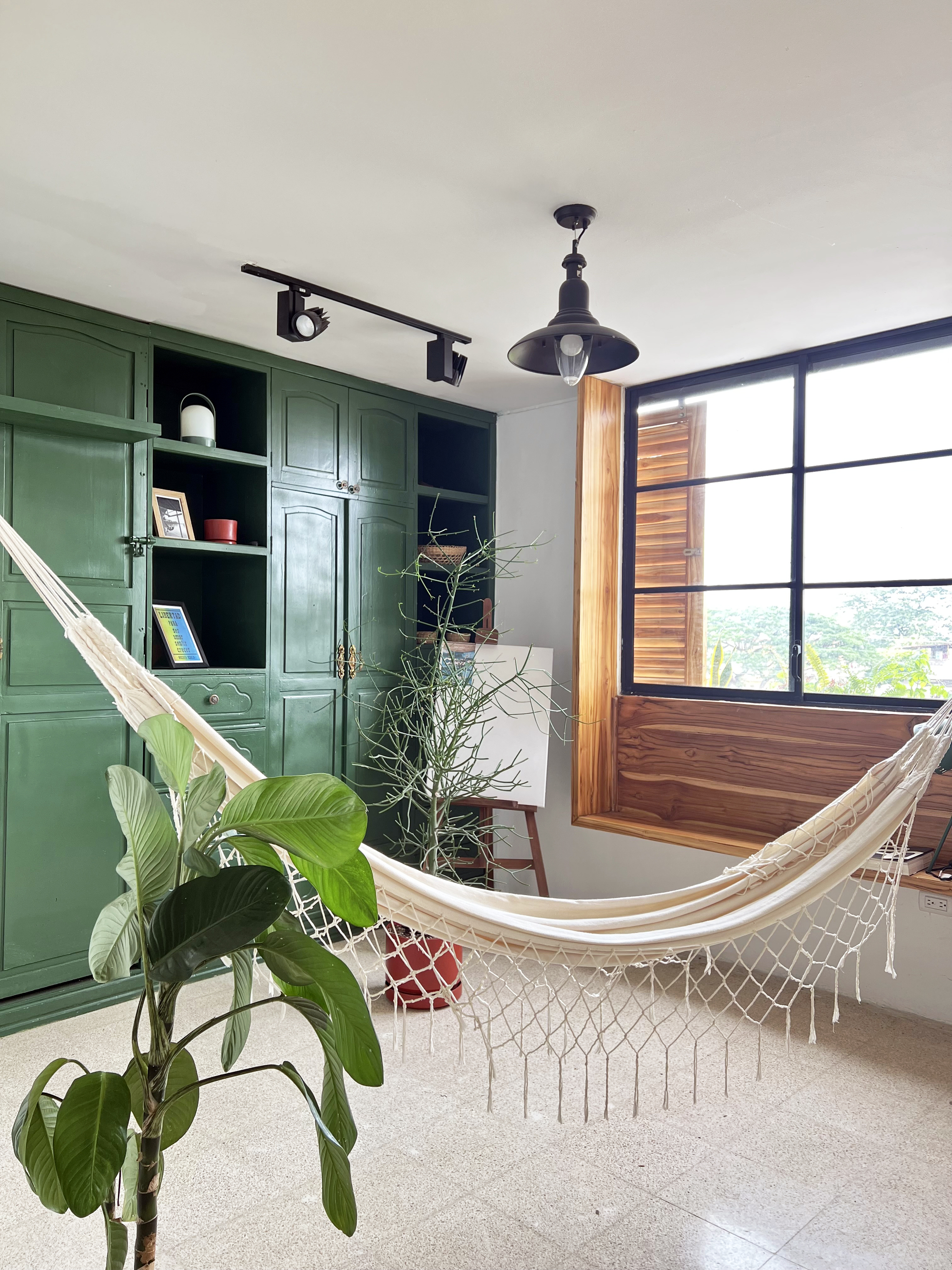 Interior room with green built-in shelving, hammock and large black-framed window overlooking greenery