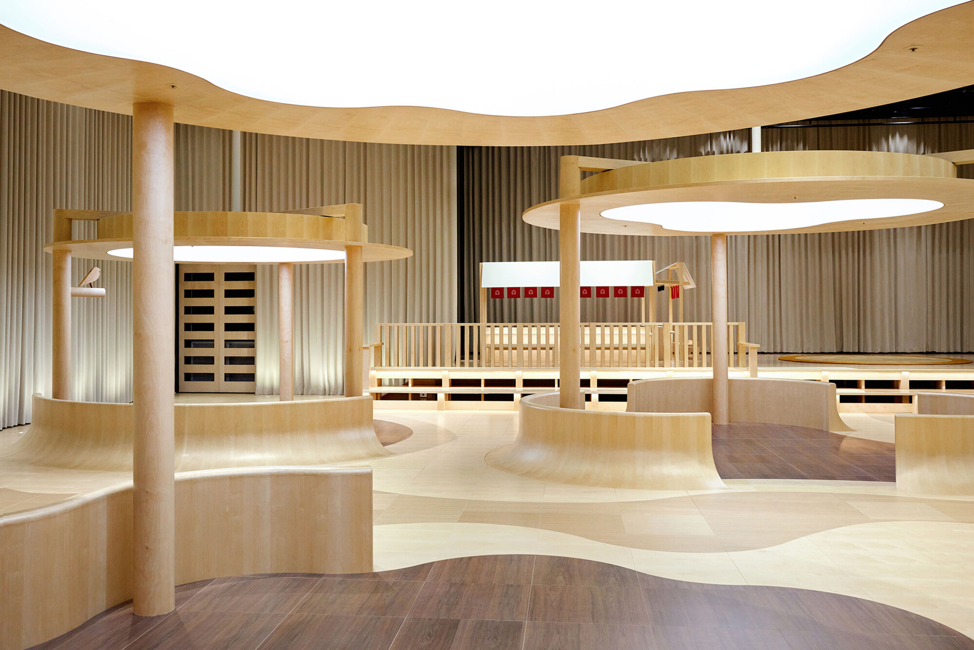 Interior view showing undulating plywood platforms with circular columns and integrated luminous ceiling rings