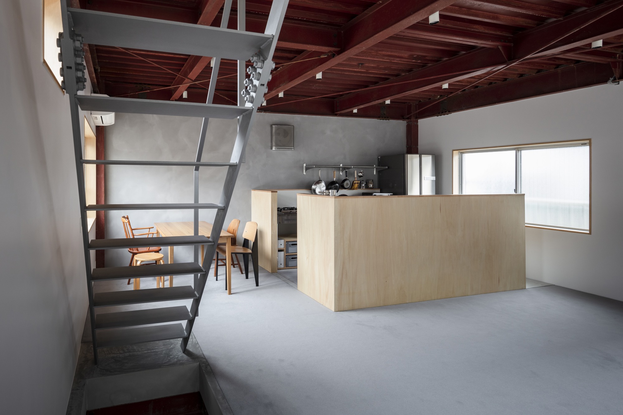 Steel staircase ascending to a loft beside a plywood kitchen island under timber rafters