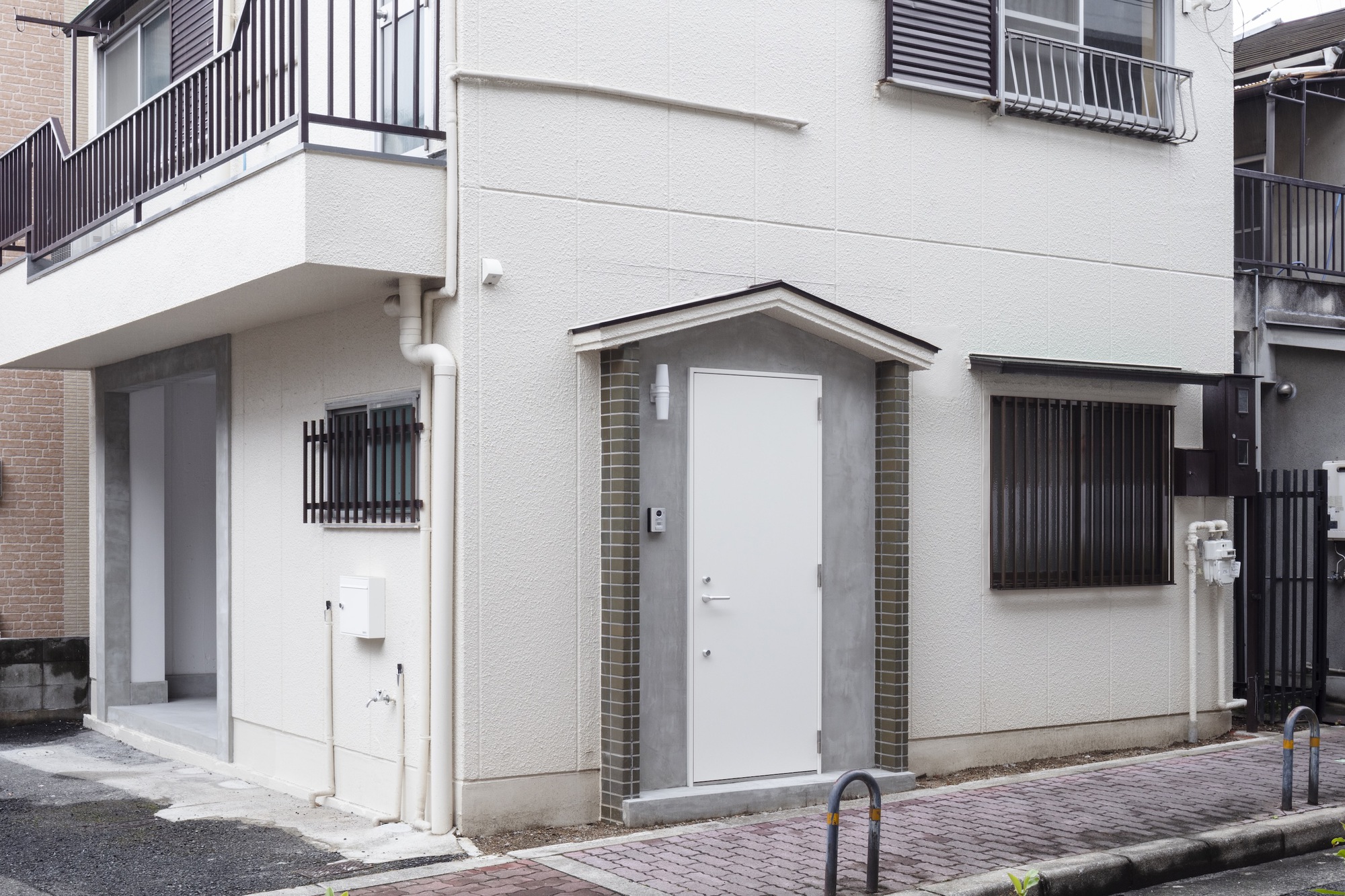 Street view of a white stucco facade with gabled entry and corrugated metal screens