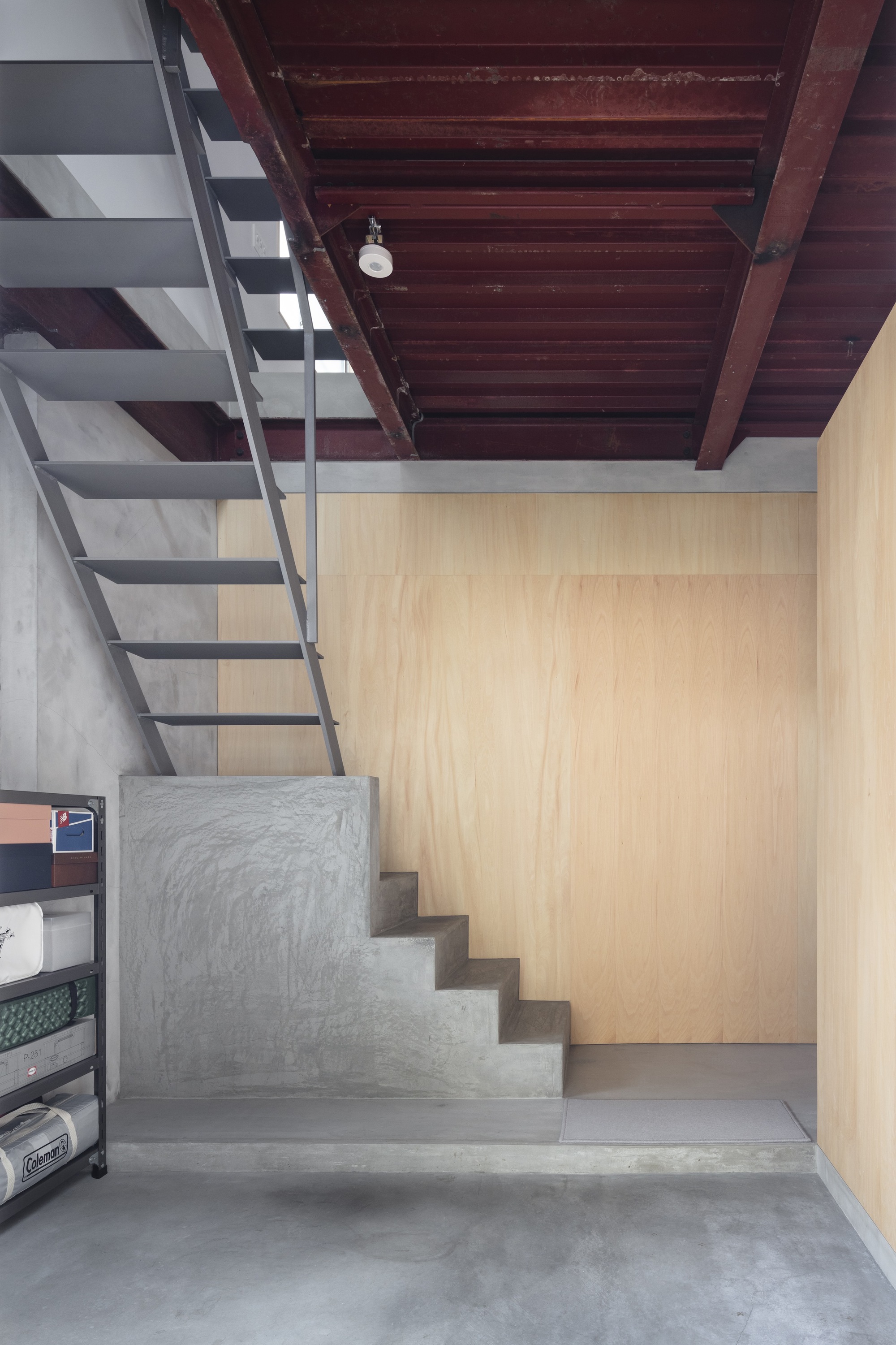 Concrete stair landing leading upward beneath dark timber ceiling and adjacent plywood wall