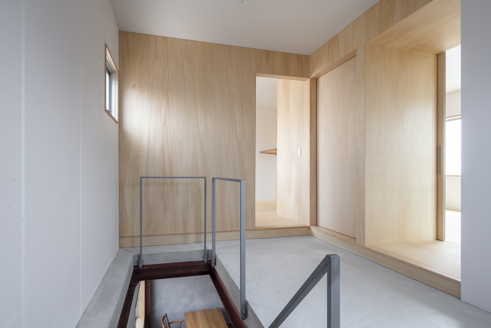 Upper hallway with pale plywood walls and glass-railed opening overlooking the space below