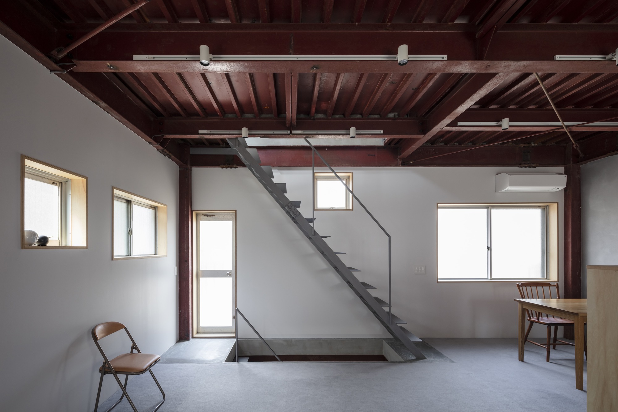 Room with diagonal steel stair crossing beneath exposed timber joists and track lighting