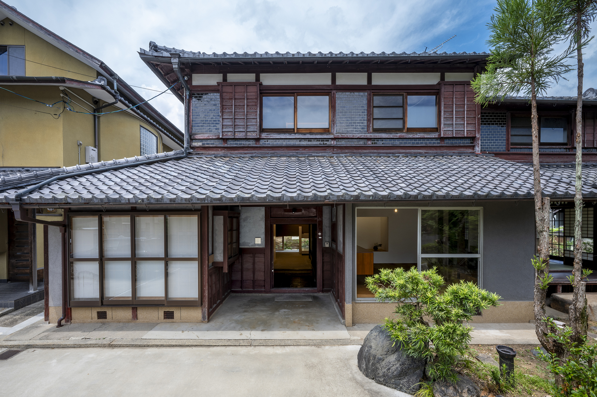 Street facade showing traditional tiled roof above timber framed windows and sliding screens with planted courtyard