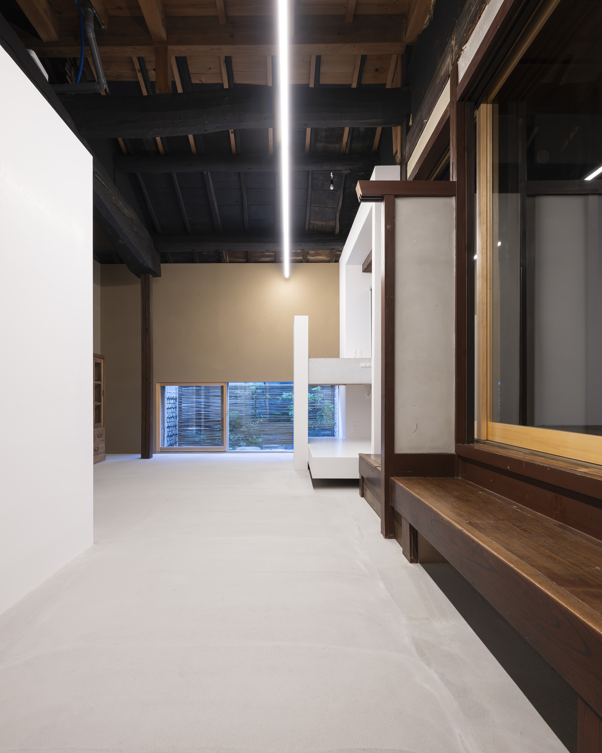 Double-height space with white mezzanine platform inserted beneath blackened timber roof structure and linear lighting