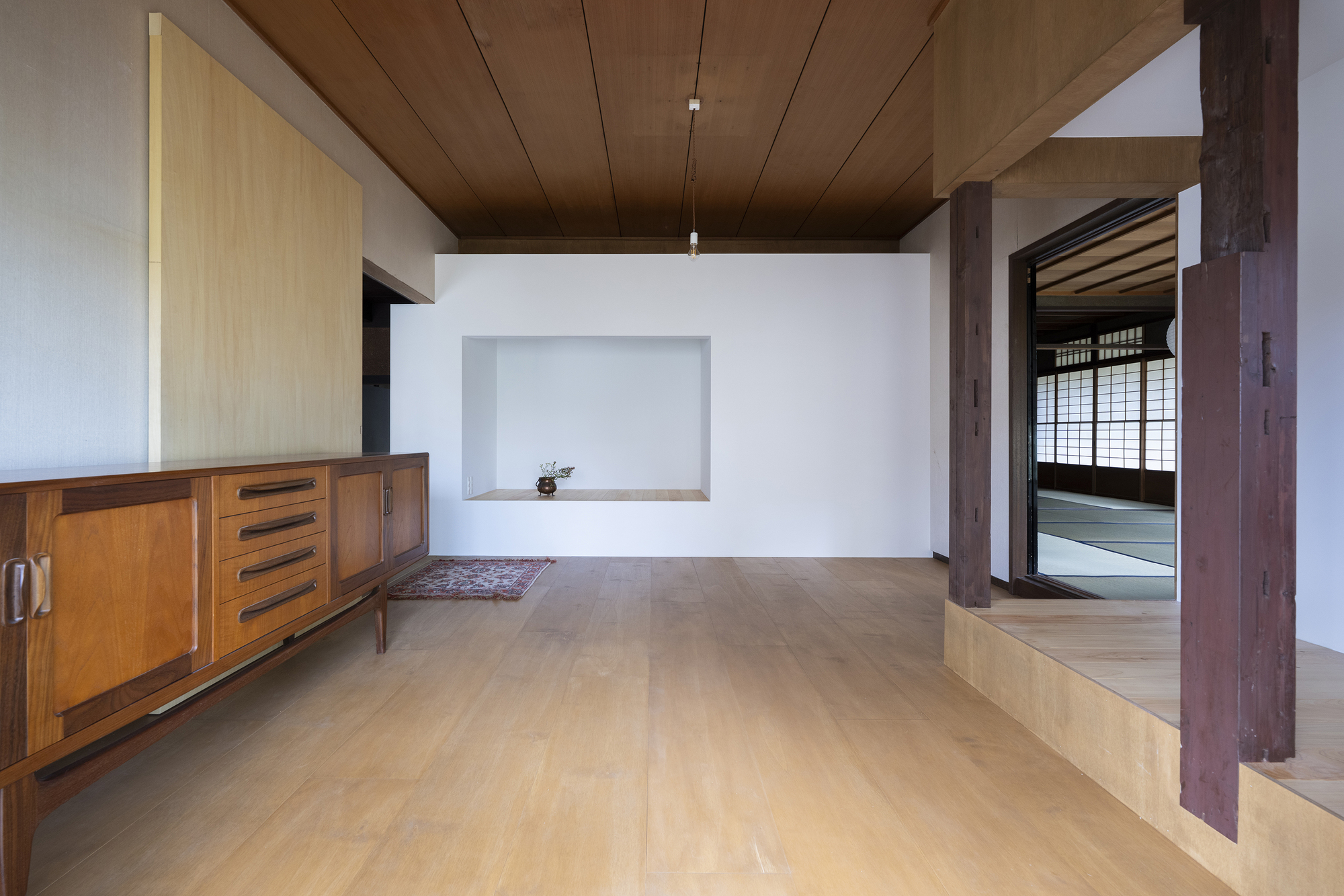 Interior room with timber ceiling, exposed wood columns and a wall niche opposite a doorway to tatami space