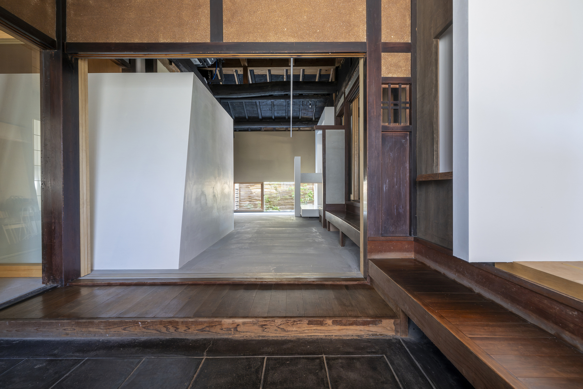 View from raised timber floor across dark stone entry threshold to polished concrete room beyond