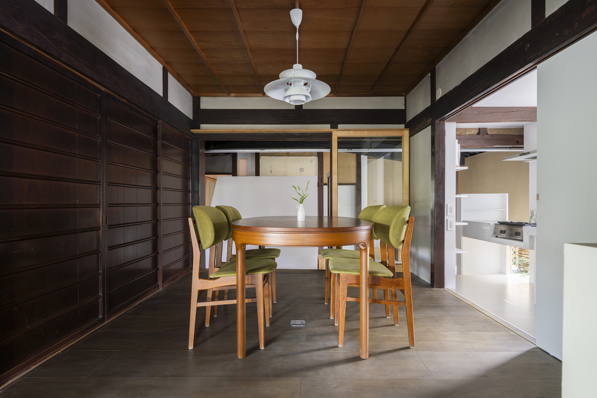 Dining area with timber table, green upholstered chairs and dark wood sliding wall panels under pendant light
