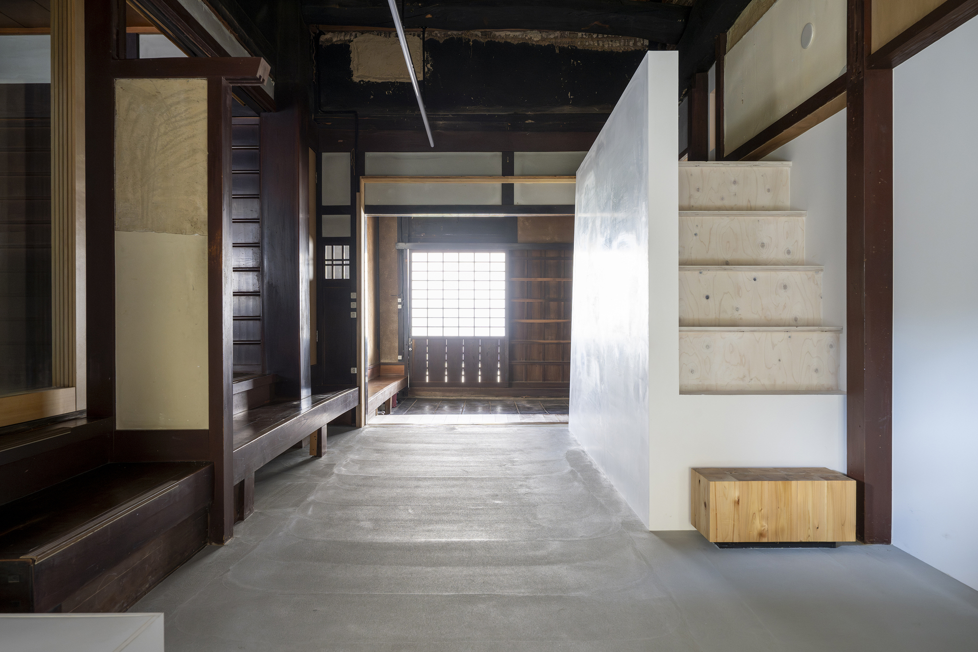 Concrete floor hallway with exposed timber structure and white plastered volumes under a dark ceiling