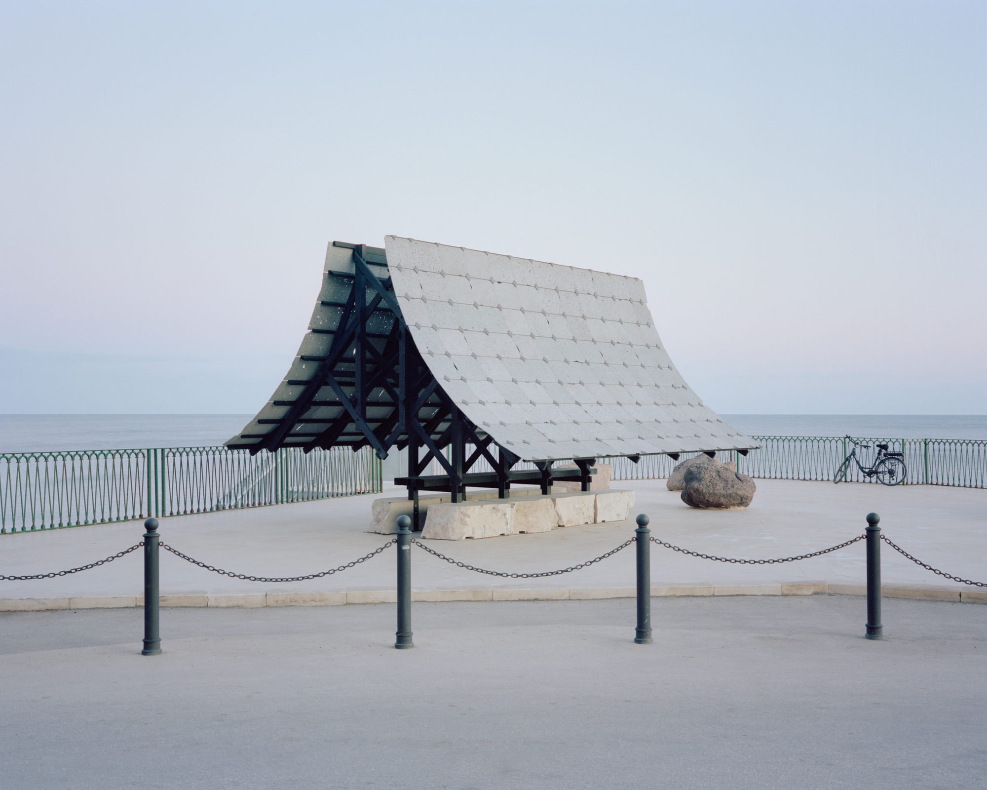 Timber pavilion with white tiled roof and exposed frame on a coastal promenade at dusk