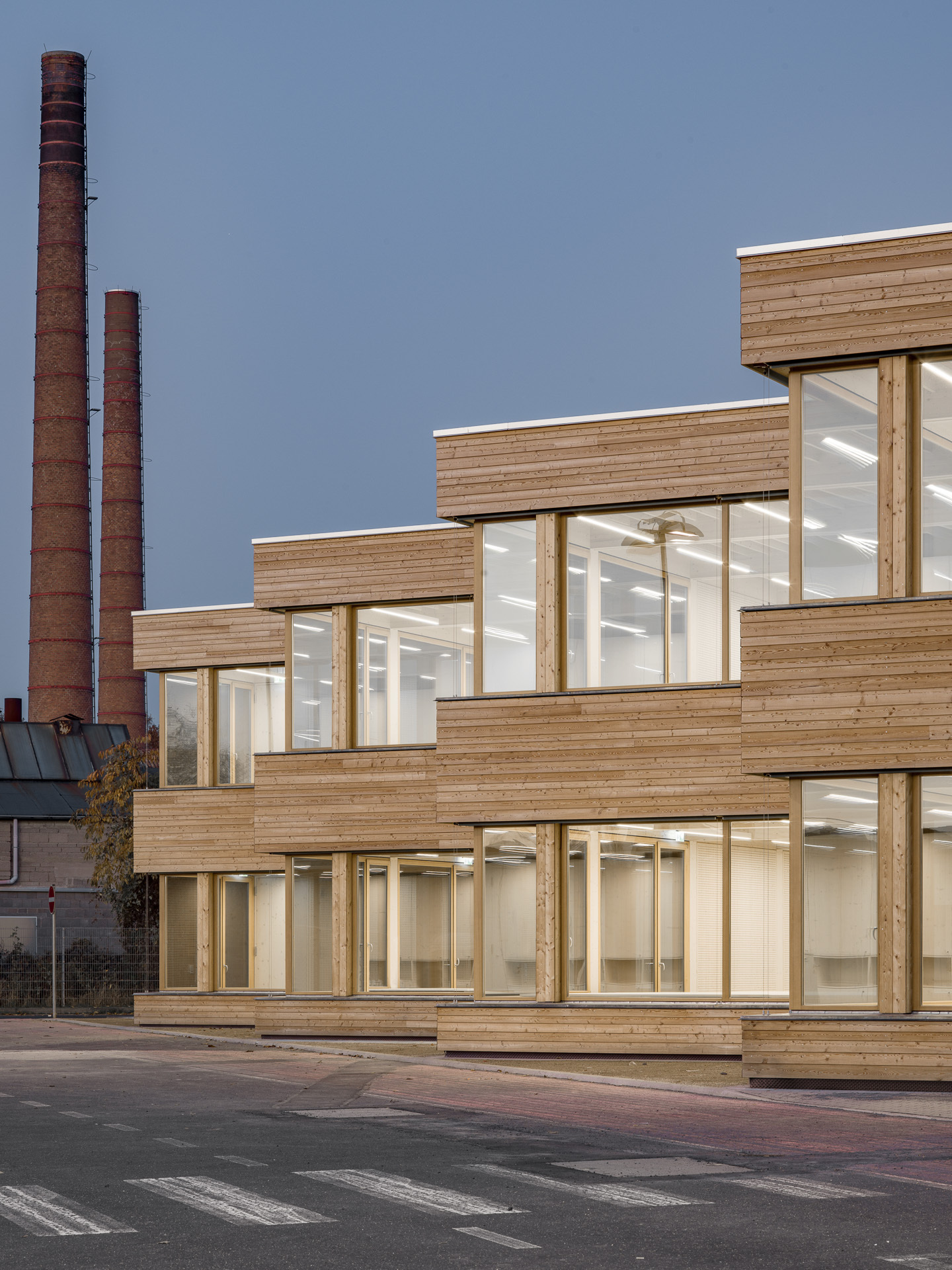 Terraced wood cladding and floor-to-ceiling glazing with industrial chimneys in the background