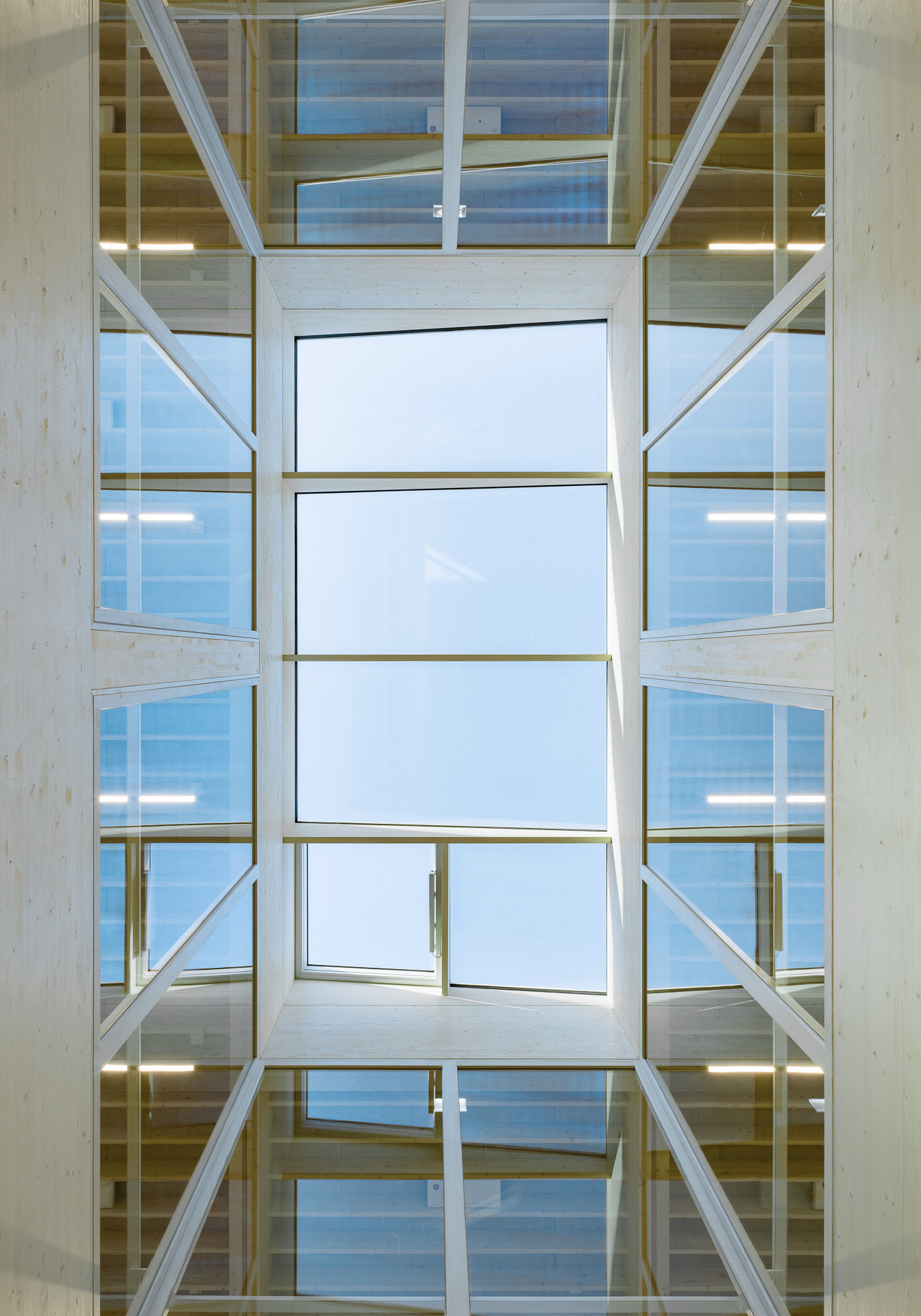 Upward view through a multi-story glazed atrium with timber beams and steel bracing